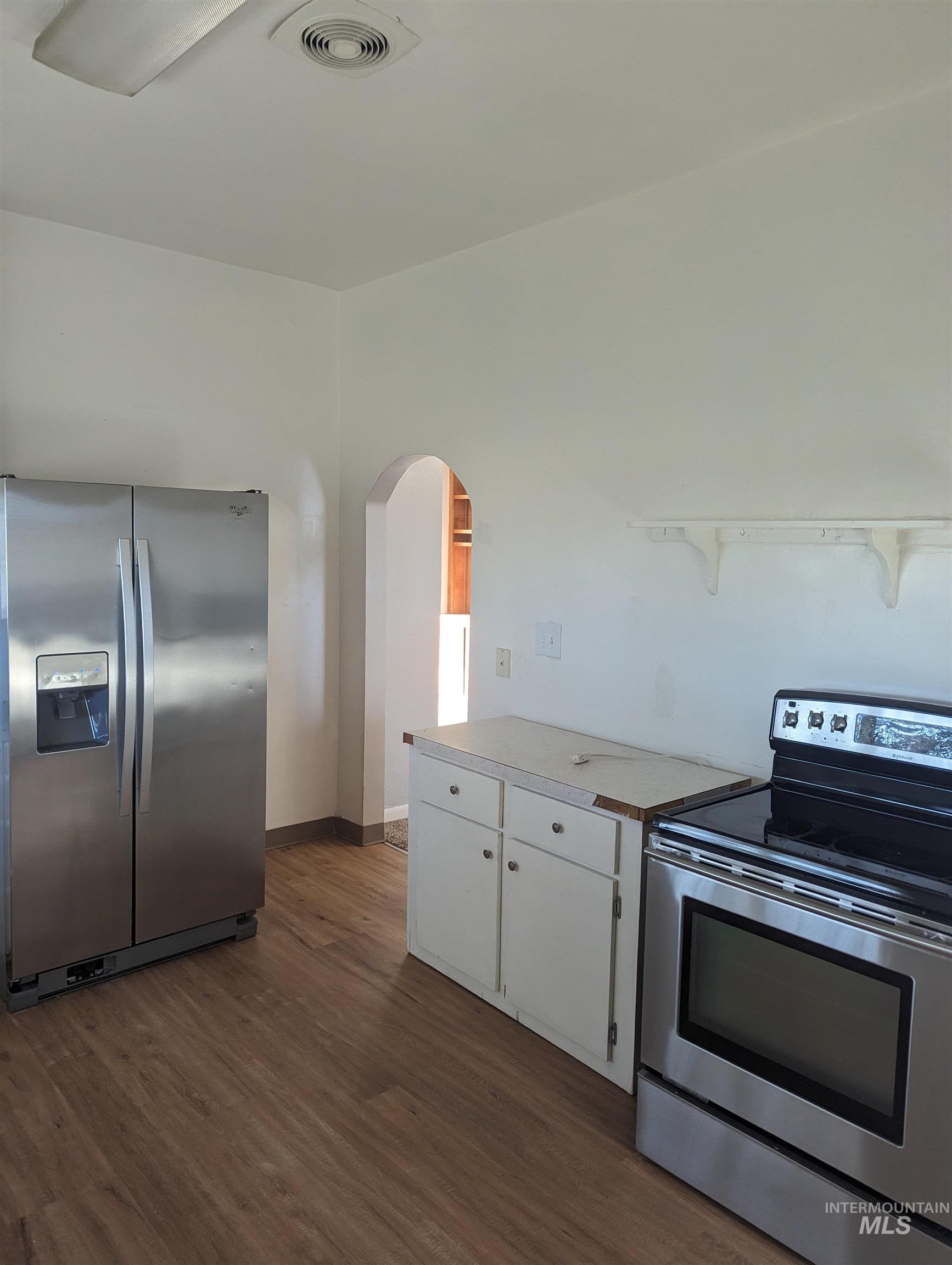 Kitchen with appliances with stainless steel finishes, white cabinetry, dark wood finished floors, light countertops, and arched walkways