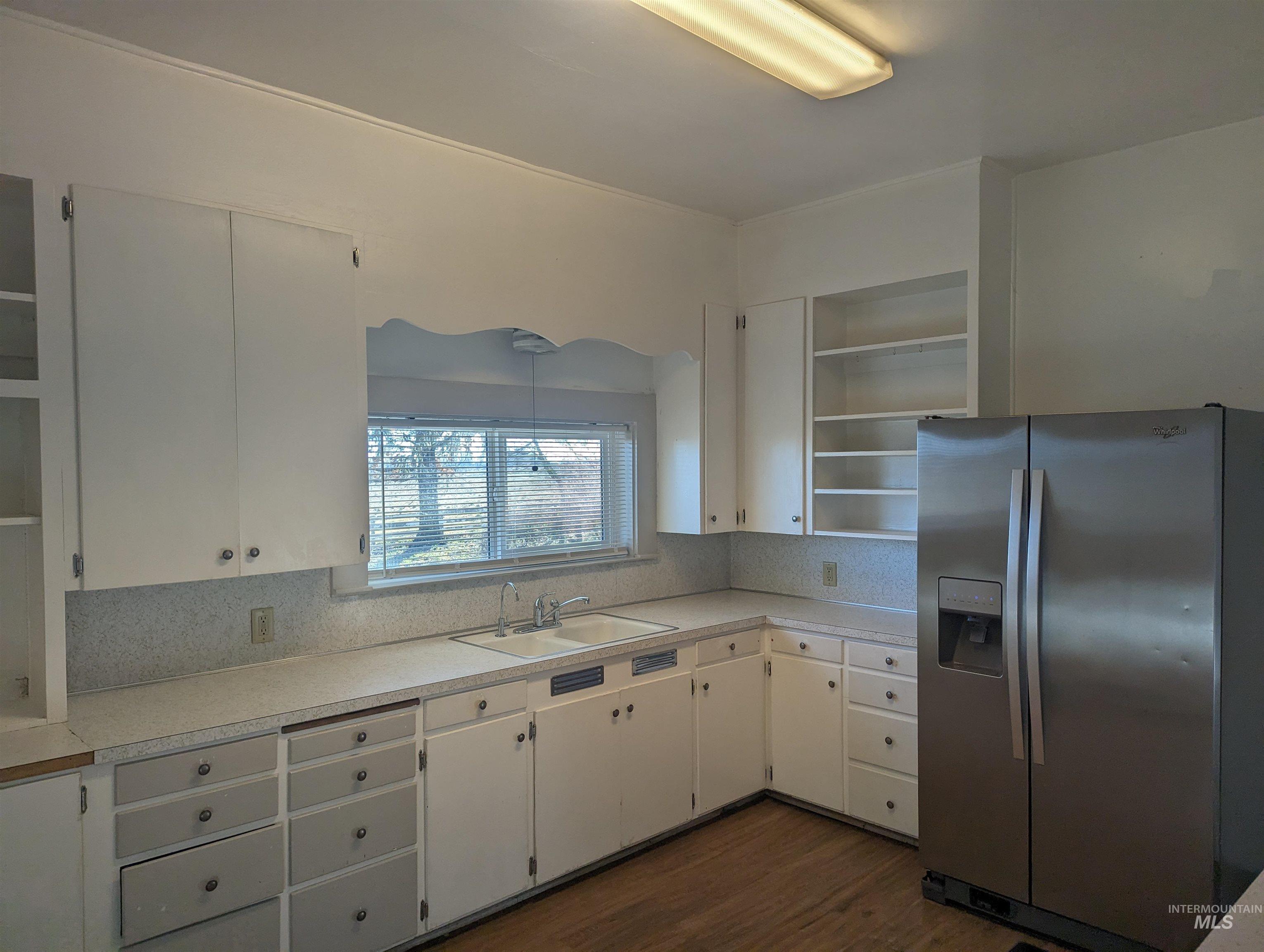 Kitchen with open shelves, stainless steel fridge with ice dispenser, light countertops, white cabinetry, and dark wood-style floors