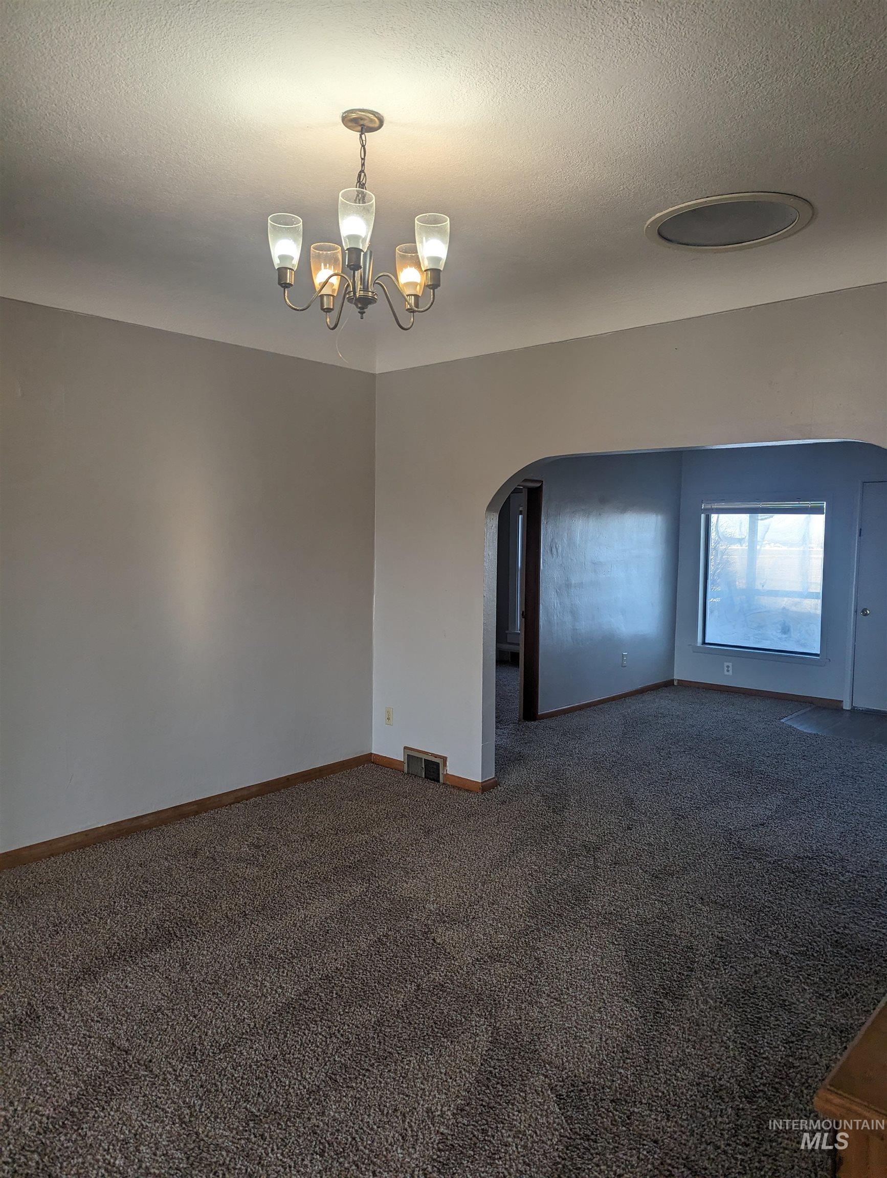 Carpeted empty room with arched walkways, a chandelier, and a textured ceiling