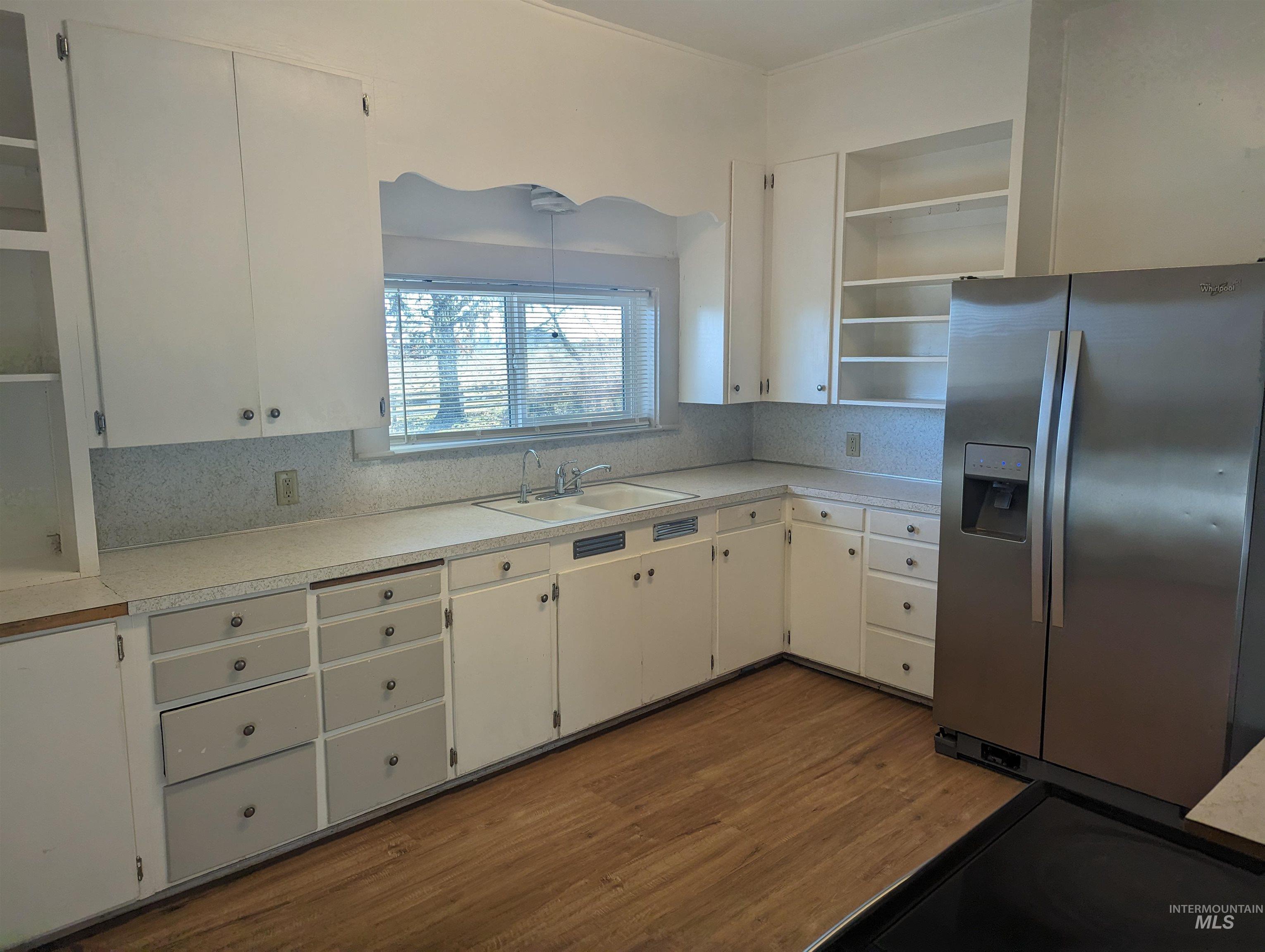 Kitchen with open shelves, stainless steel fridge with ice dispenser, light countertops, and white cabinets