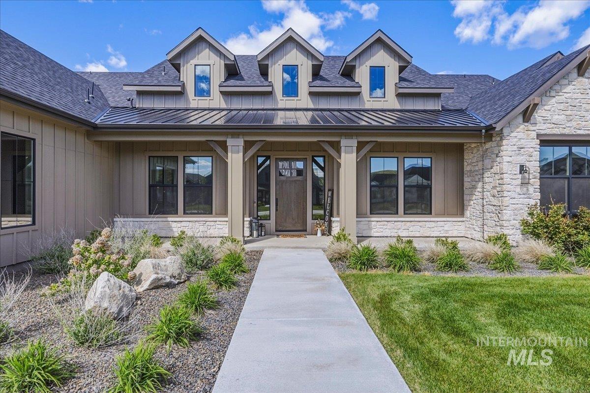 Contemporary farmhouse-style exterior featuring board and batten siding, natural stone accents, a dark metal roof, and gabled dormers