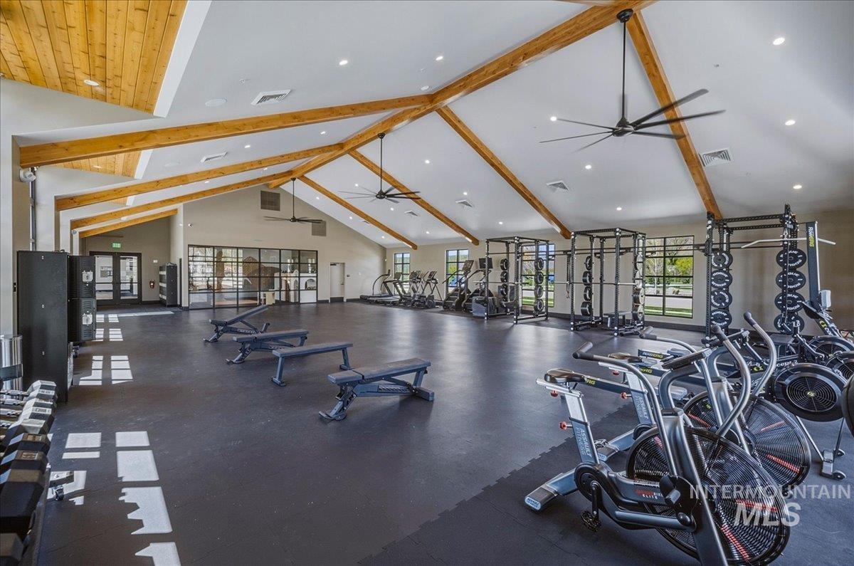Spacious fitness center featuring vaulted ceilings with exposed wood beams, large industrial-style ceiling fans, and extensive window-lined walls