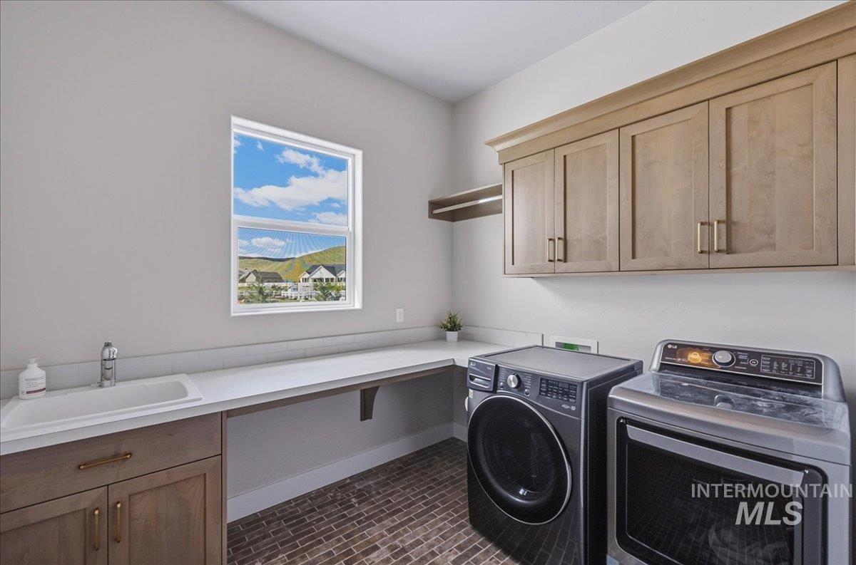 Laundry area featuring wood-finish cabinetry, a white rectangular sink, light-toned countertops, and brick-patterned flooring