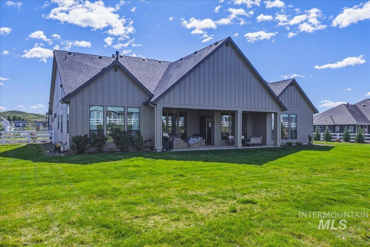 Expansive lawn surrounding a contemporary-style home with a covered patio, multiple large windows, and a dark shingle roof