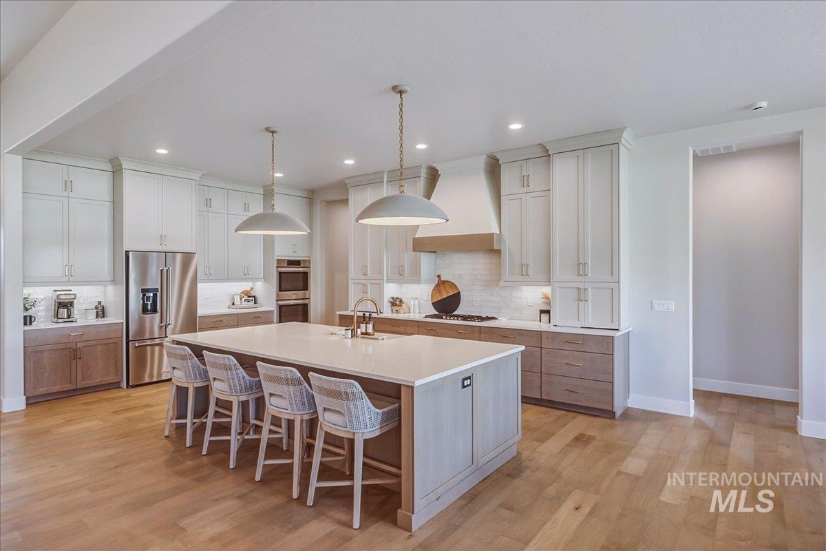 Spacious kitchen featuring a large central island with seating, stainless steel appliances, upper white cabinetry, lower wood-finish cabinetry, and recessed lighting