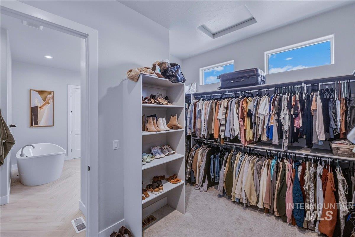 Walk-in closet featuring extensive built-in shelving and hanging rods, overhead windows, and a recessed ceiling light