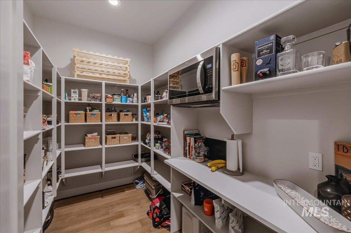 Spacious walk-in pantry featuring extensive white shelving, wood-finish flooring, recessed lighting, and a built-in microwave