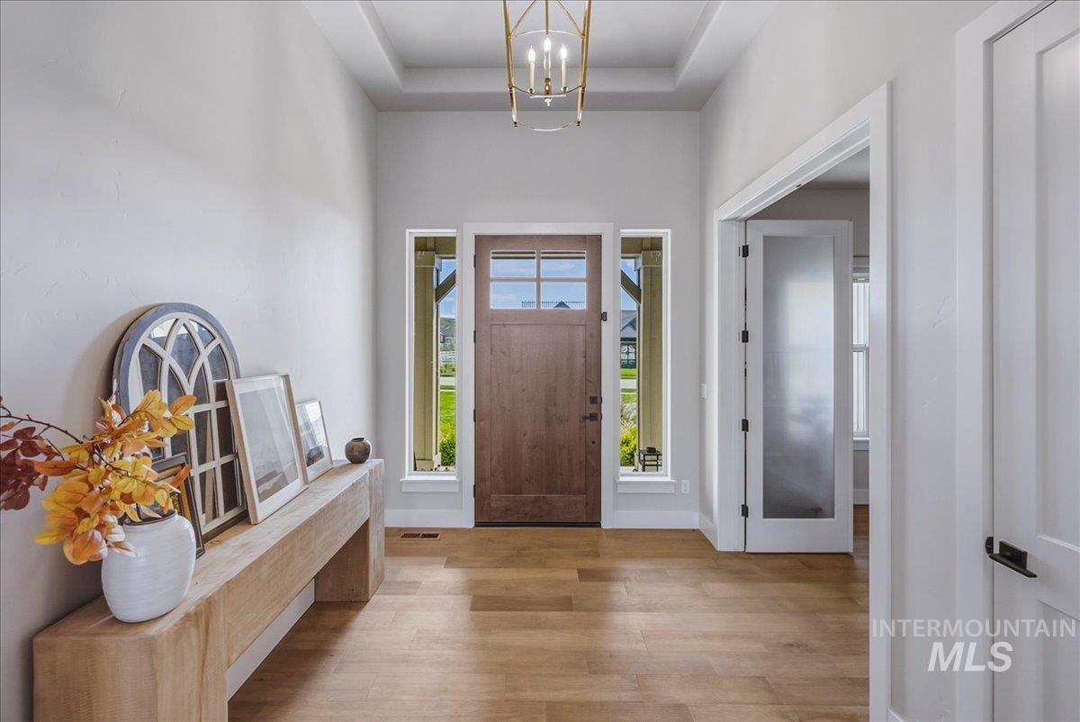 Entry foyer featuring wood-finish flooring, a tray ceiling with a contemporary chandelier, and a wood entry door flanked by sidelight windows