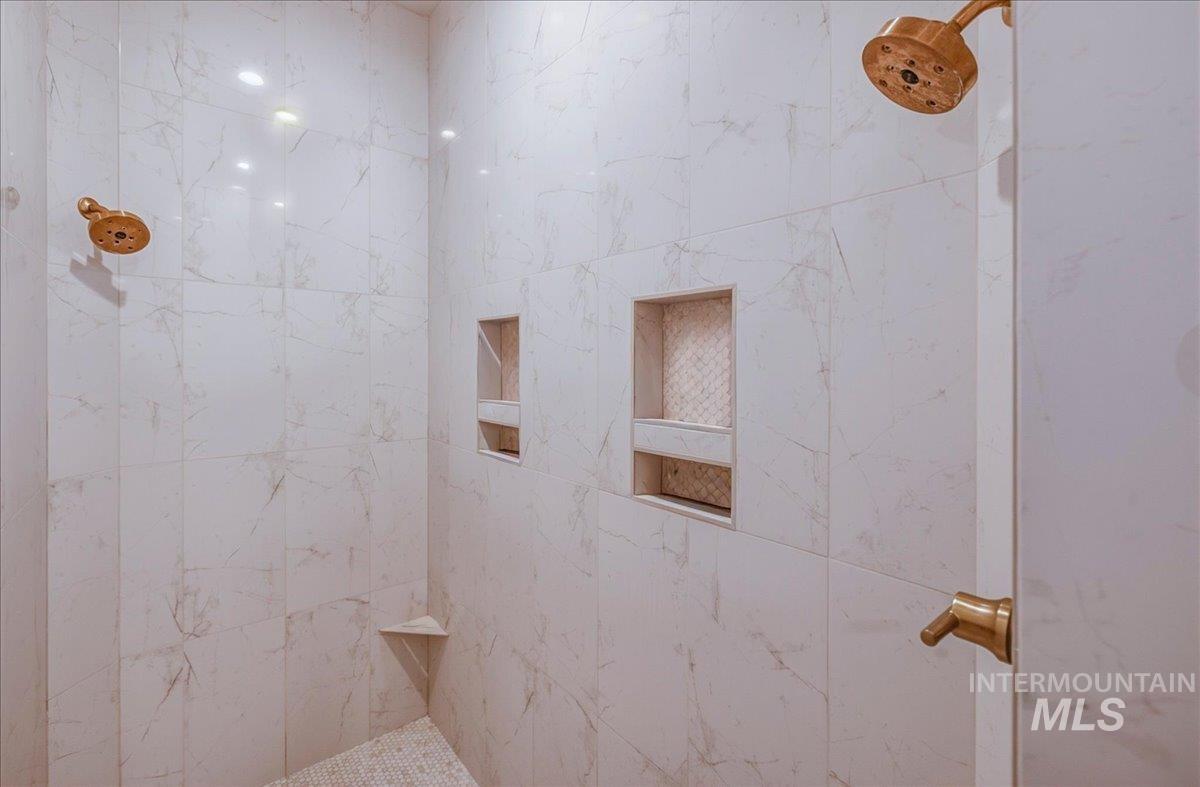 Shower with large format white tile walls, dual showerheads, two recessed niches, and a corner shelf