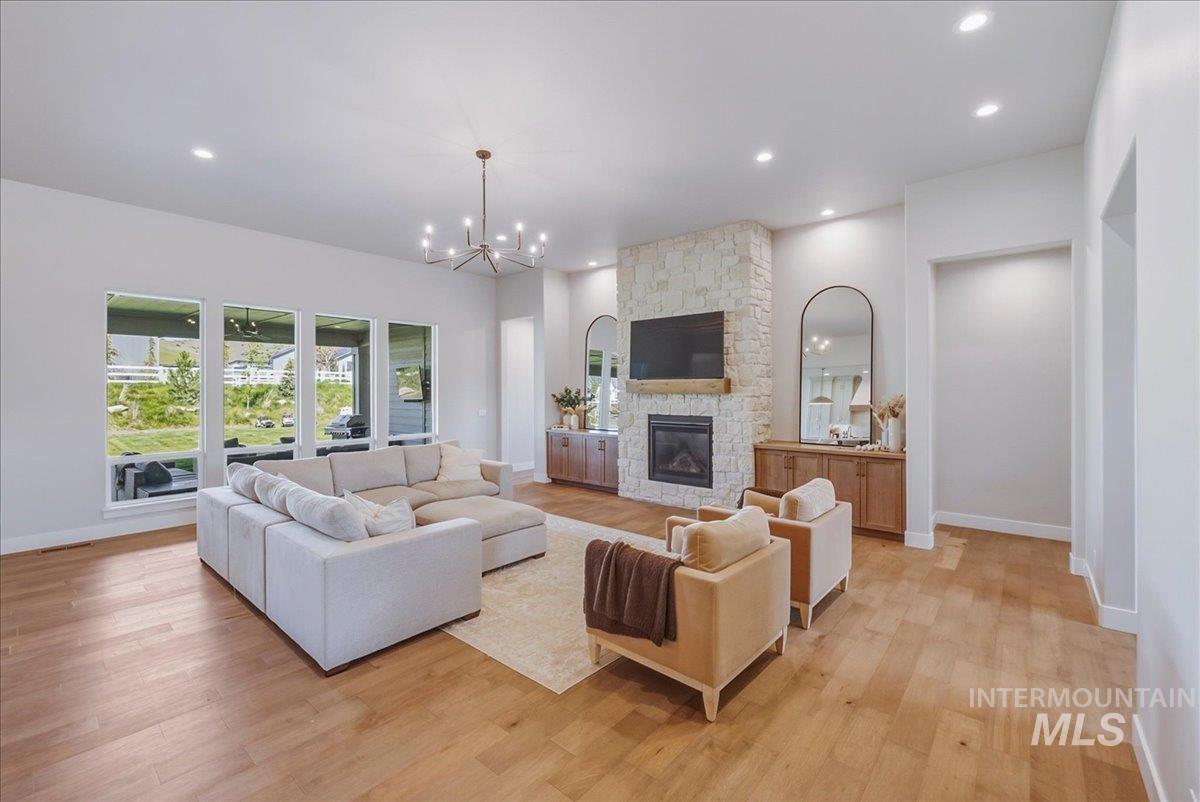 Open-concept living space featuring wood-finish flooring, a stone-clad fireplace with a wood mantle, and recessed lighting