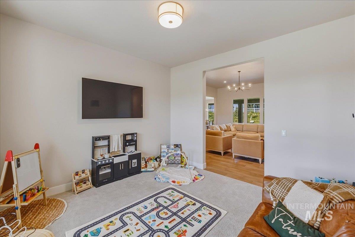 Carpeted room with a wall-mounted display, recessed lighting, and a wide entryway to a hardwood-floored living area