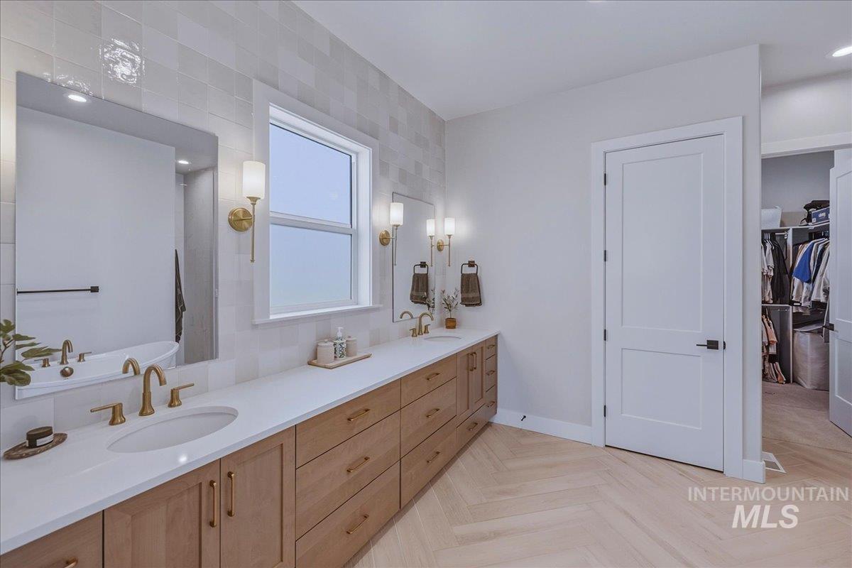 Dual vanity with white countertops and undermount sinks, wood-finish cabinetry, brushed brass fixtures, and a herringbone-patterned flooring