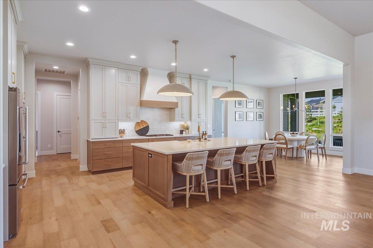 Spacious kitchen featuring an expansive island with seating for five, wood-finish flooring, two-tone cabinetry, stainless steel appliances, and a dining area with large windows