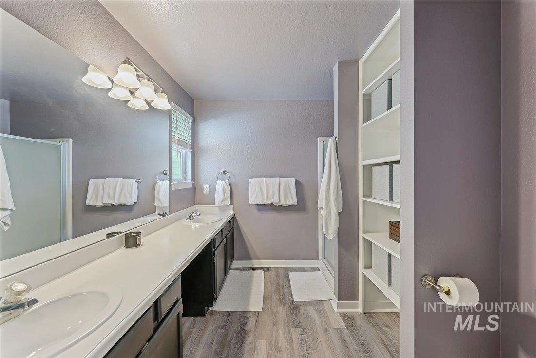 Full bath featuring wood finished floors, a stall shower, double vanity, and a textured ceiling