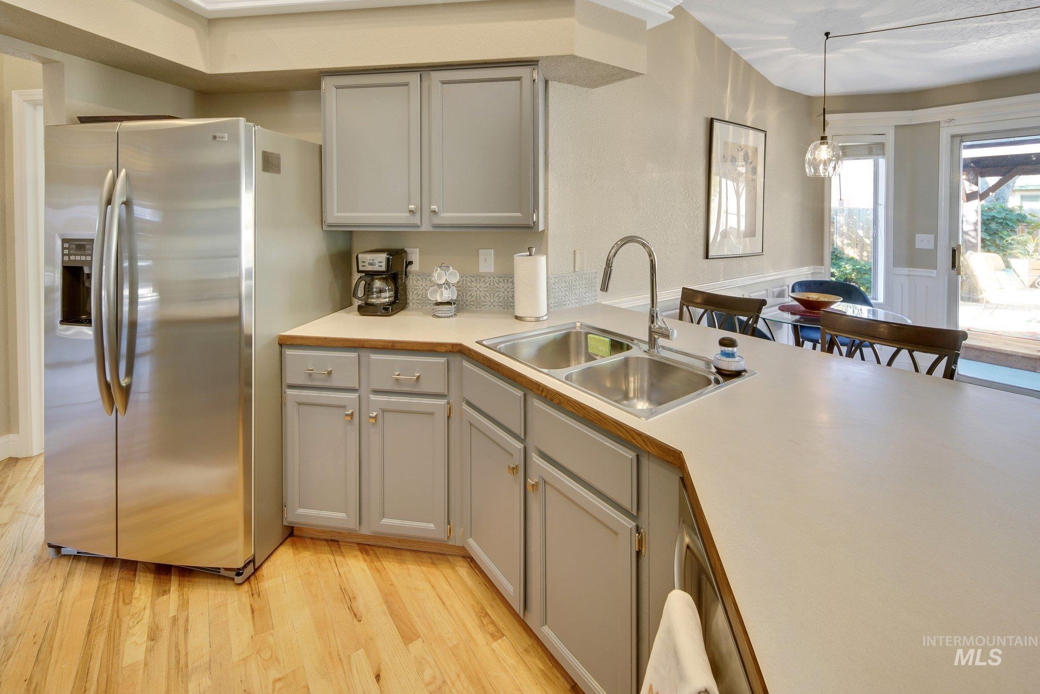 Kitchen featuring light countertops, gray cabinetry, stainless steel fridge, and light wood-style floors