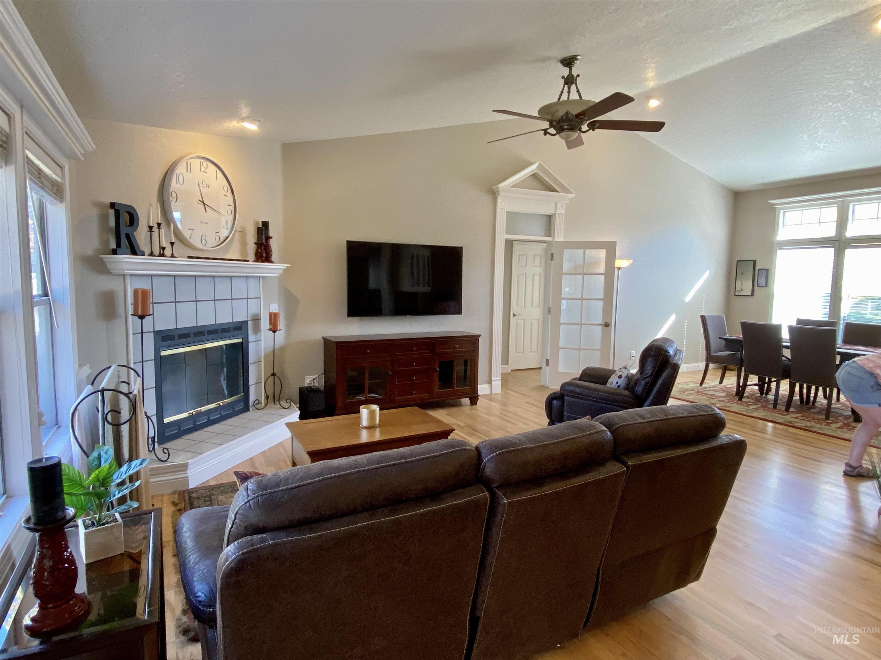 Living area with lofted ceiling, a tiled fireplace, light wood finished floors, a ceiling fan, and a textured ceiling
