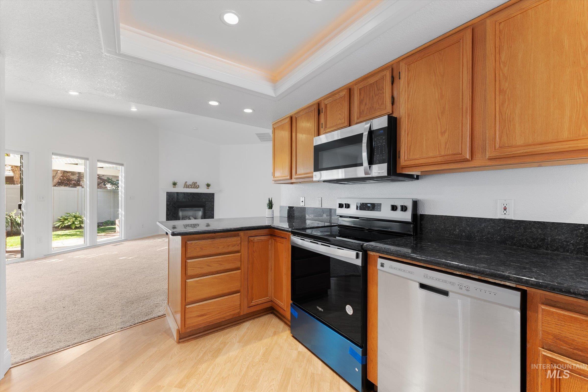 Kitchen with a peninsula, appliances with stainless steel finishes, a raised ceiling, open floor plan, and recessed lighting