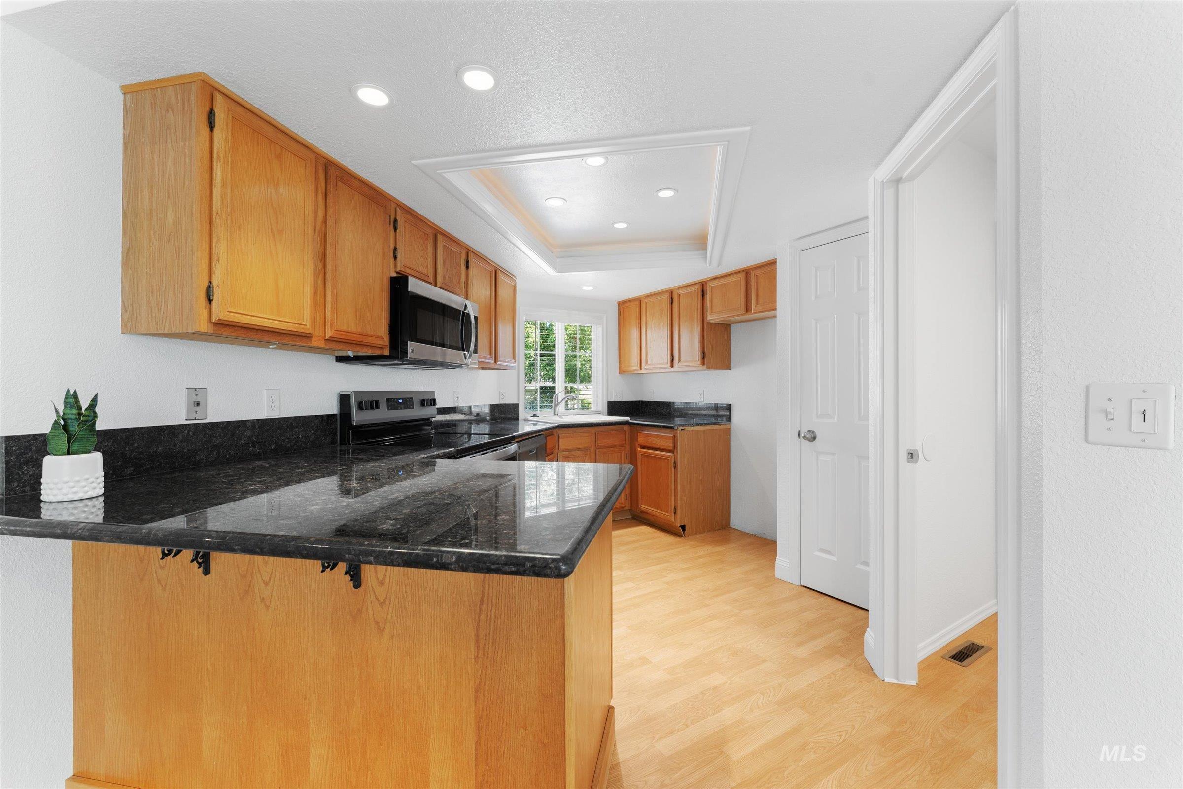 Kitchen featuring light wood-style floors, a peninsula, a breakfast bar, brown cabinets, and stainless steel appliances