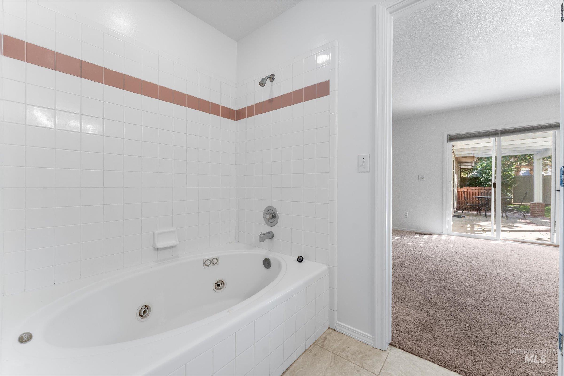 Bathroom with a combined bath / shower with jetted tub, light tile patterned flooring, and a textured ceiling