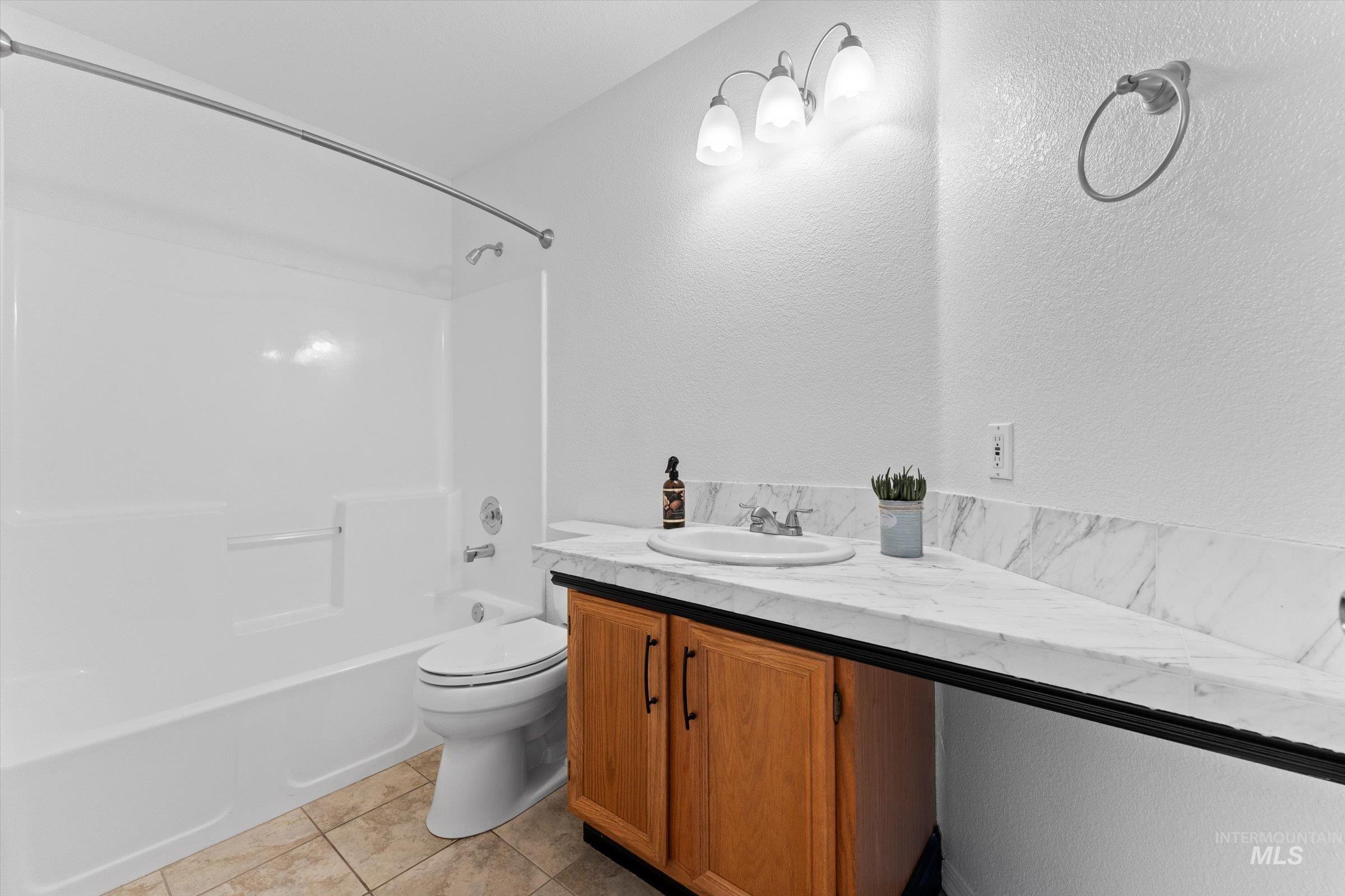 Full bathroom with washtub / shower combination, vanity, light tile patterned floors, and a textured wall