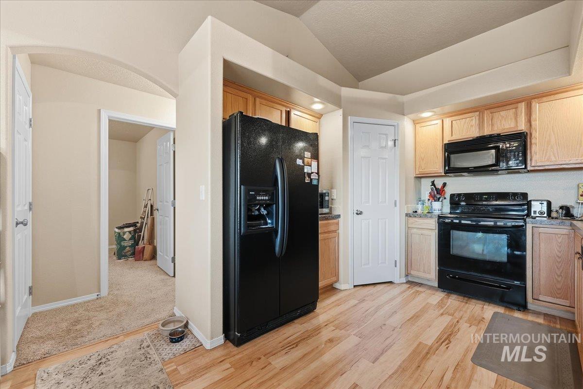 Kitchen with black appliances, light wood-style floors, light brown cabinetry, and lofted ceiling