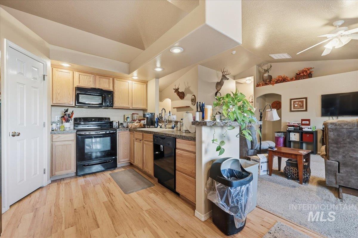 Kitchen featuring open floor plan, black appliances, vaulted ceiling, light wood finished floors, and recessed lighting