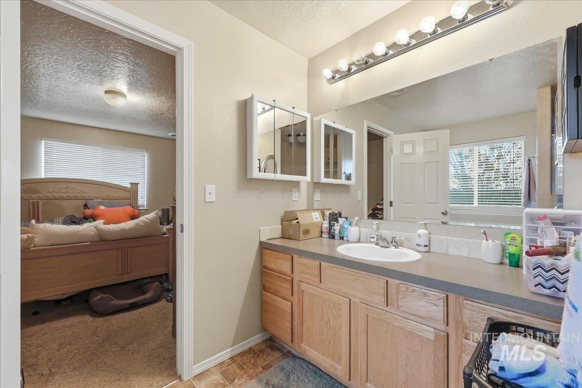 Ensuite bathroom featuring a textured ceiling, vanity, and light colored carpet