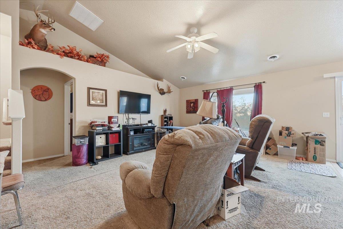 Living room featuring lofted ceiling, carpet, arched walkways, a textured ceiling, and a ceiling fan