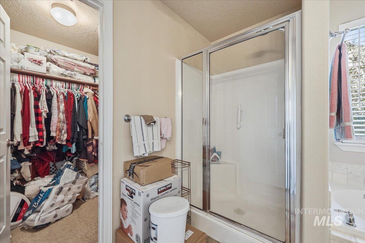 Full bathroom featuring a spacious closet, a shower stall, a textured ceiling, and a bath