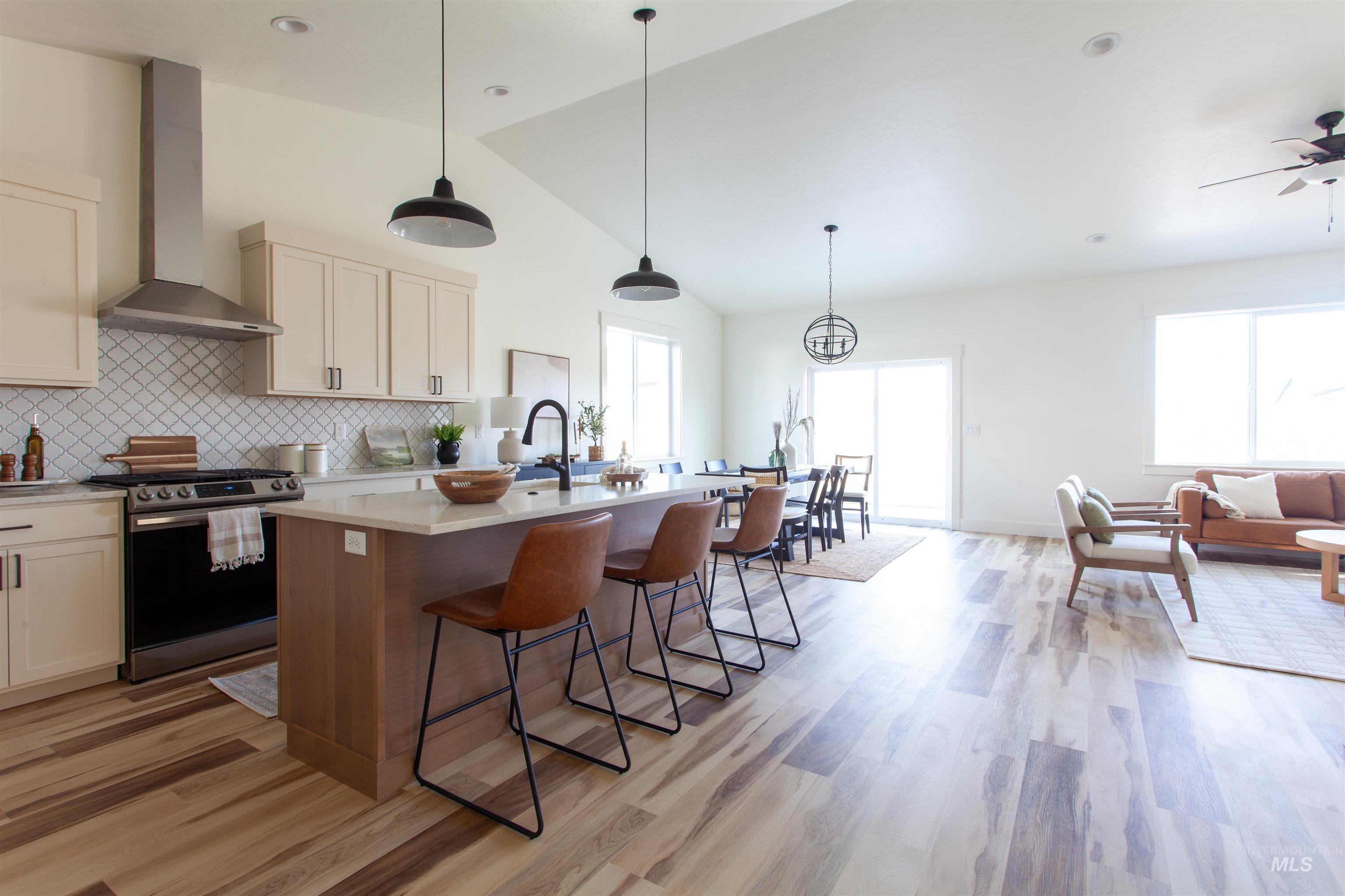 Kitchen with stainless steel gas range, pendant lighting, wall chimney range hood, tasteful backsplash, and high vaulted ceiling