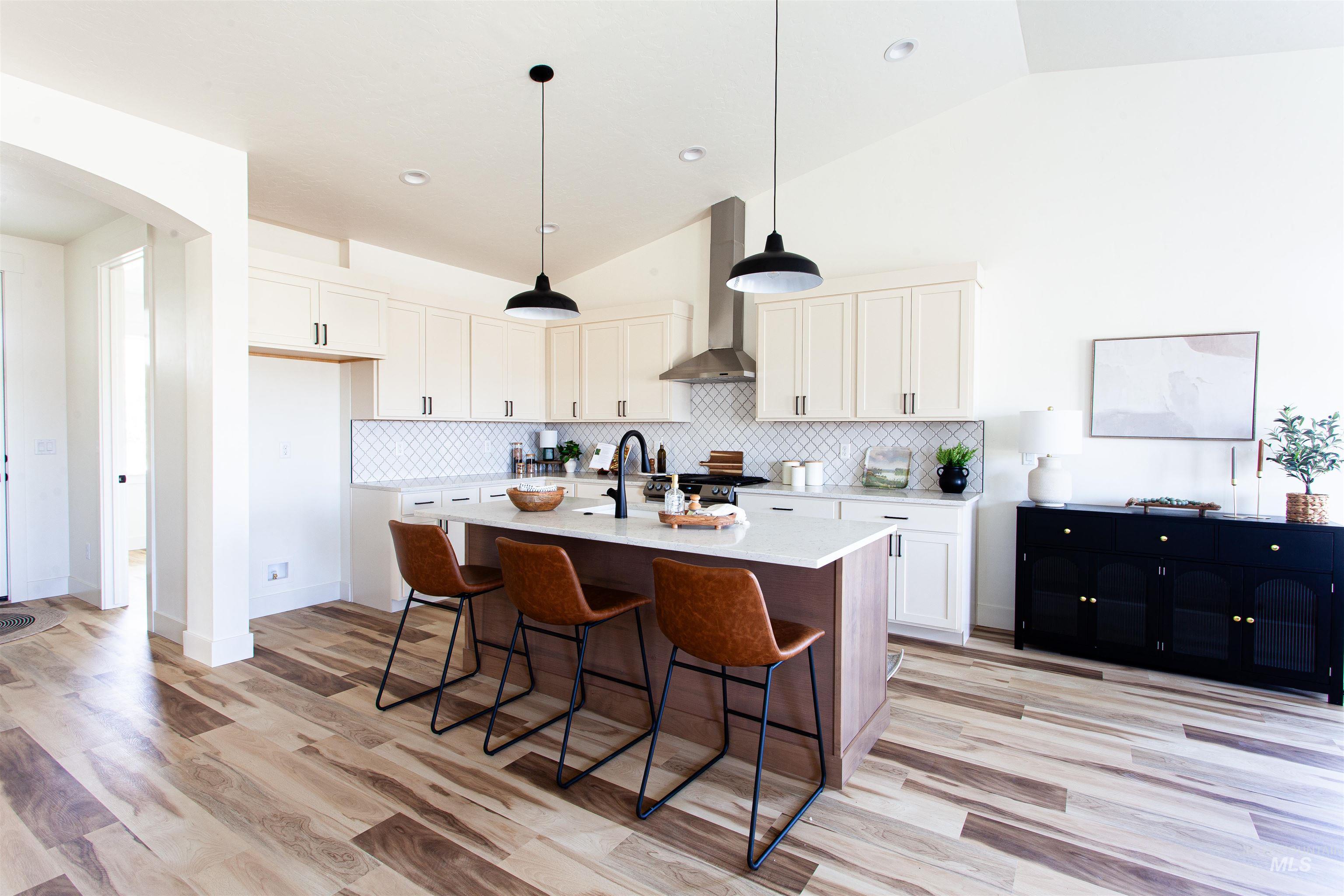 Kitchen featuring backsplash, hanging light fixtures, a kitchen bar, arched walkways, and a kitchen island with sink