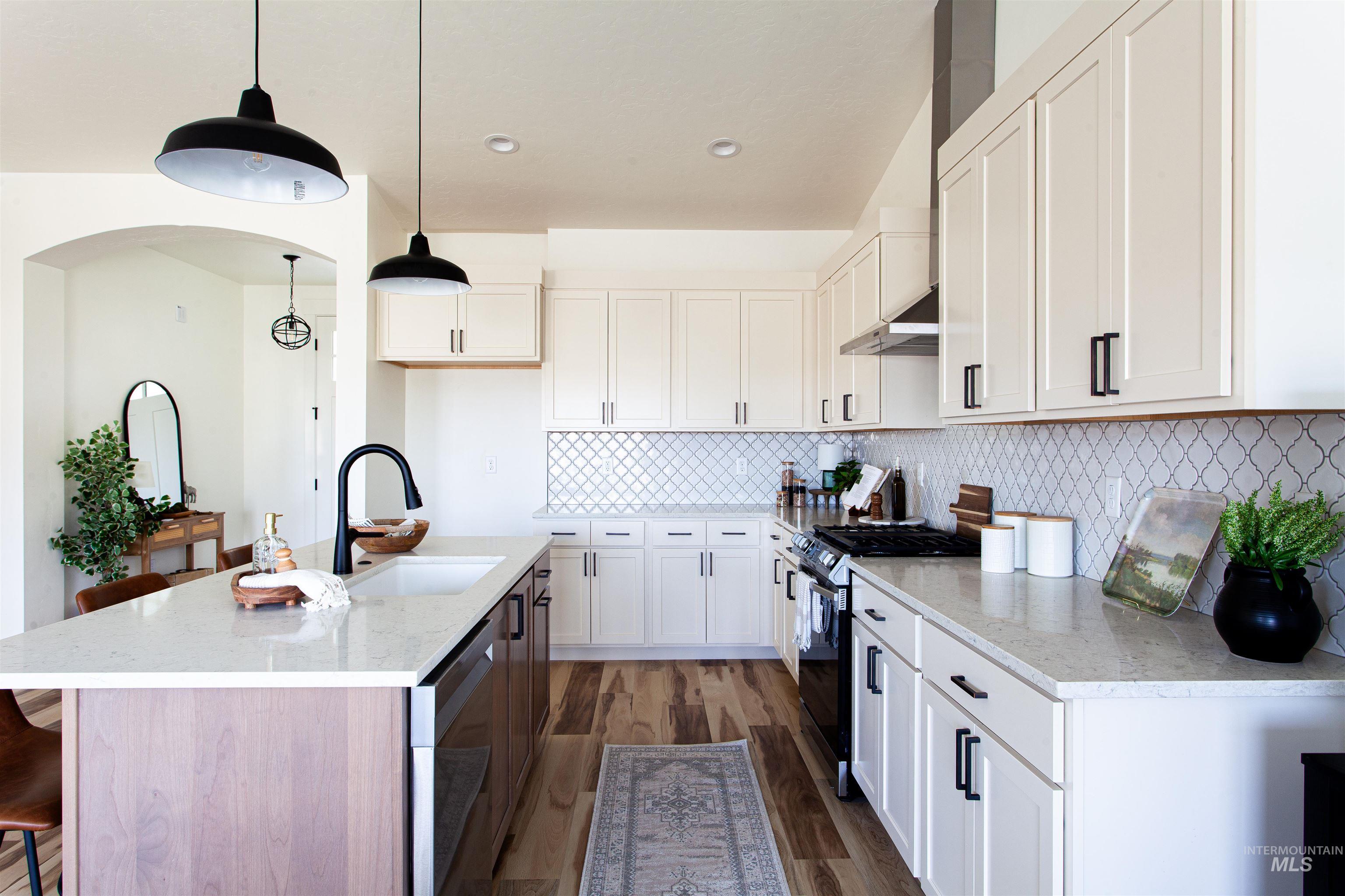 Kitchen with a kitchen breakfast bar, gas range, wall chimney range hood, dark wood-type flooring, and pendant lighting