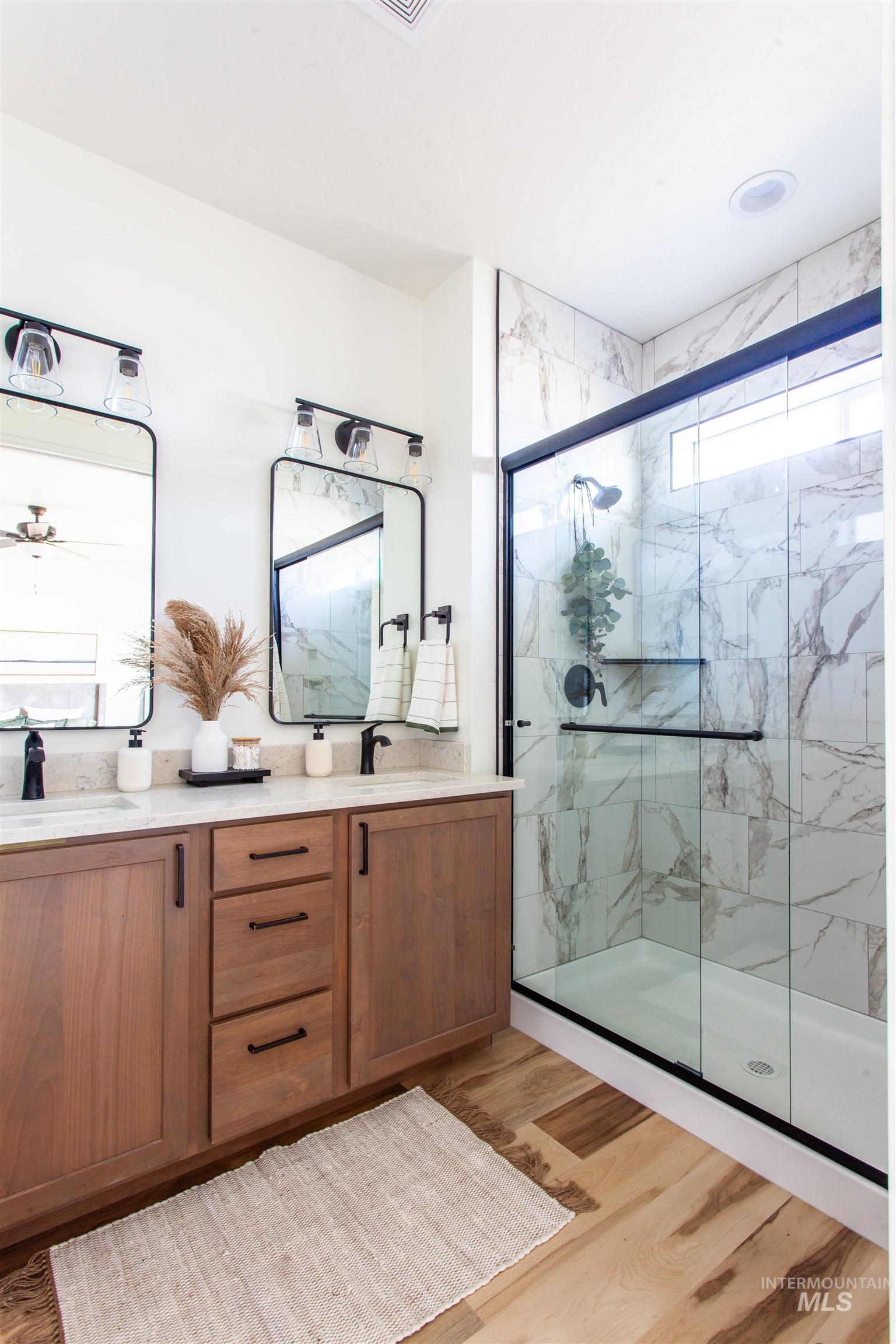 Full bathroom featuring double vanity, a marble finish shower, and light wood-type flooring