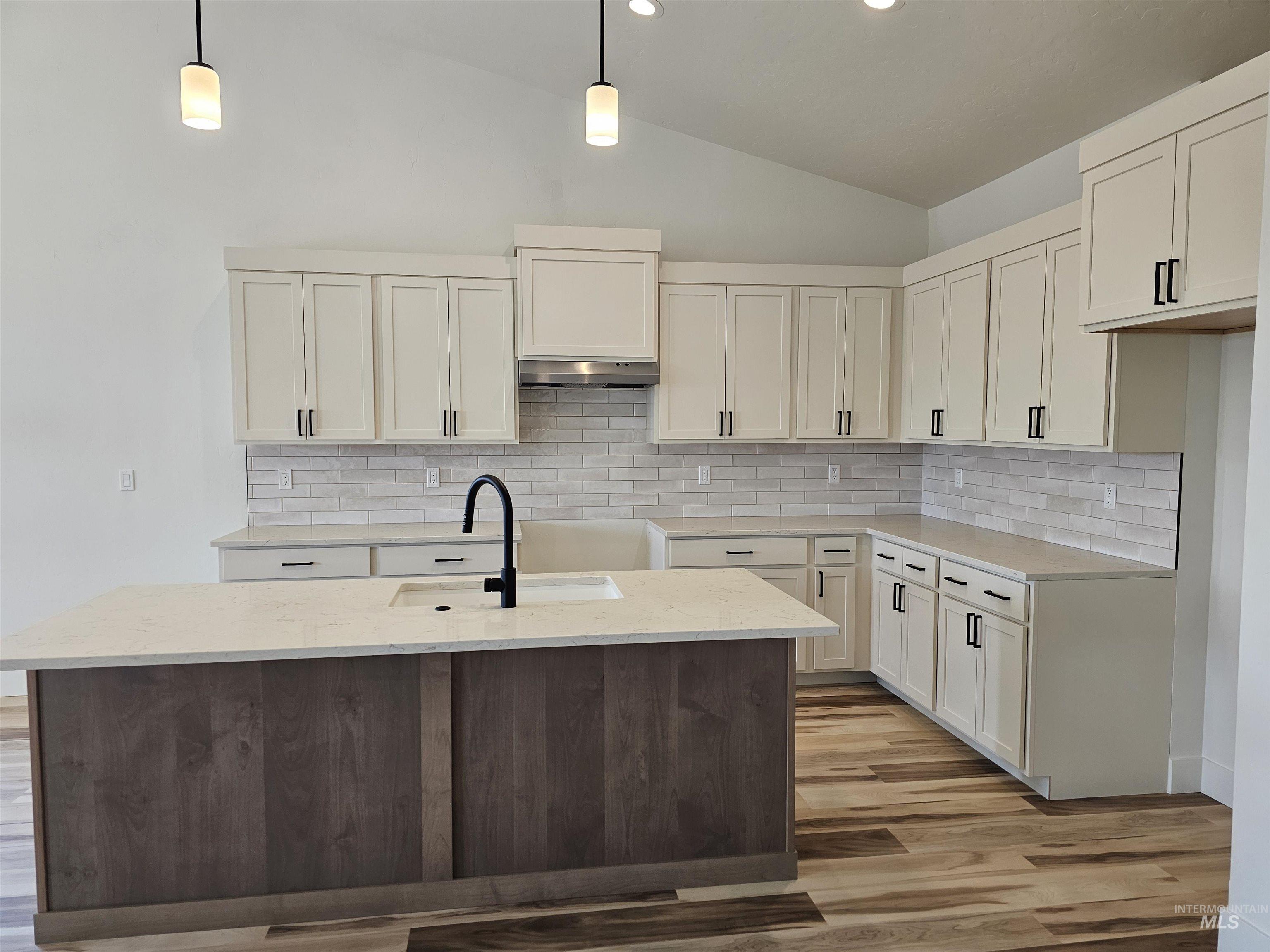Kitchen with lofted ceiling, pendant lighting, light stone counters, light wood finished floors, and white cabinetry