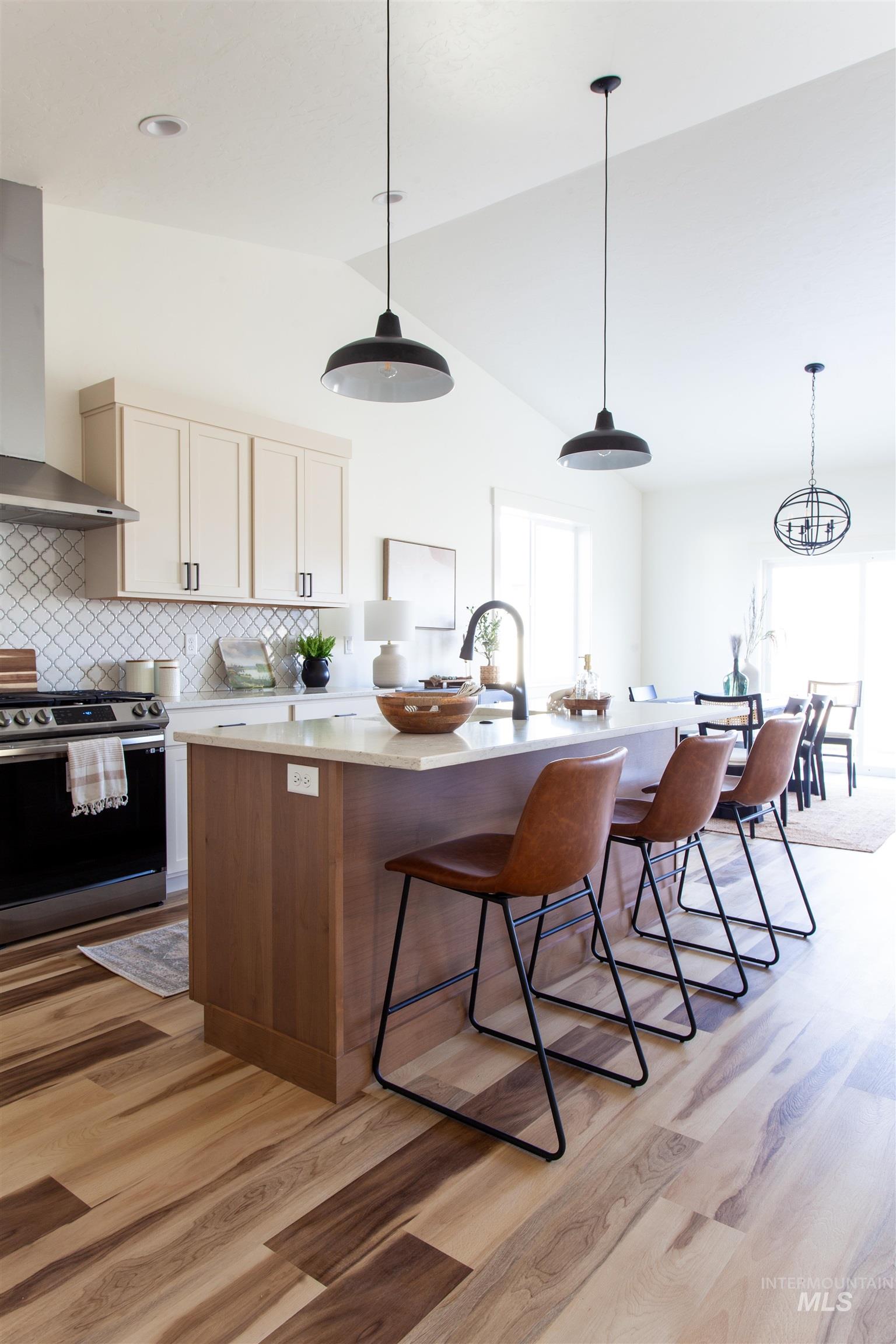 Kitchen featuring decorative light fixtures, gas stove, wall chimney exhaust hood, a center island with sink, and a kitchen breakfast bar
