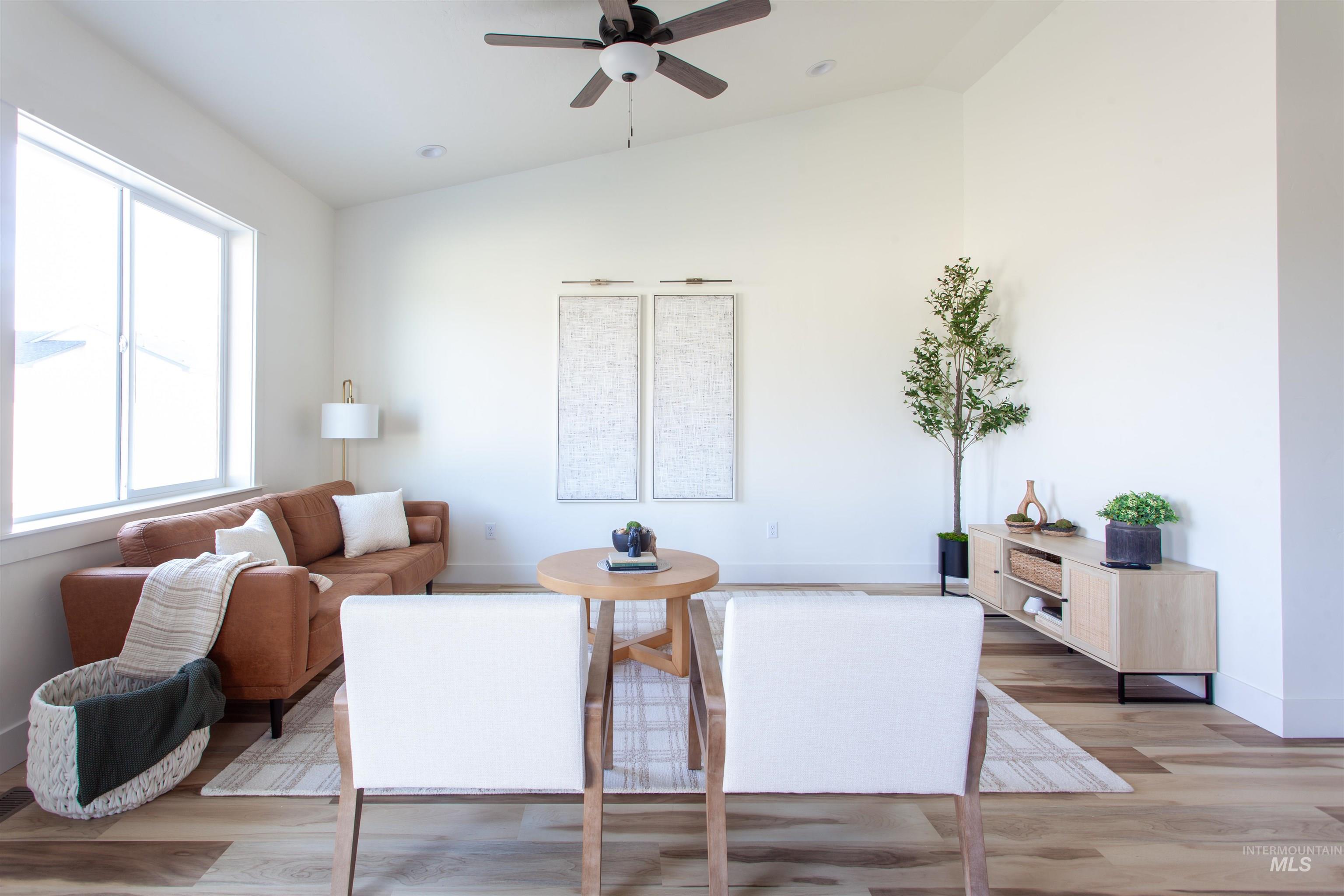 Living area featuring vaulted ceiling, light wood-style flooring, and ceiling fan