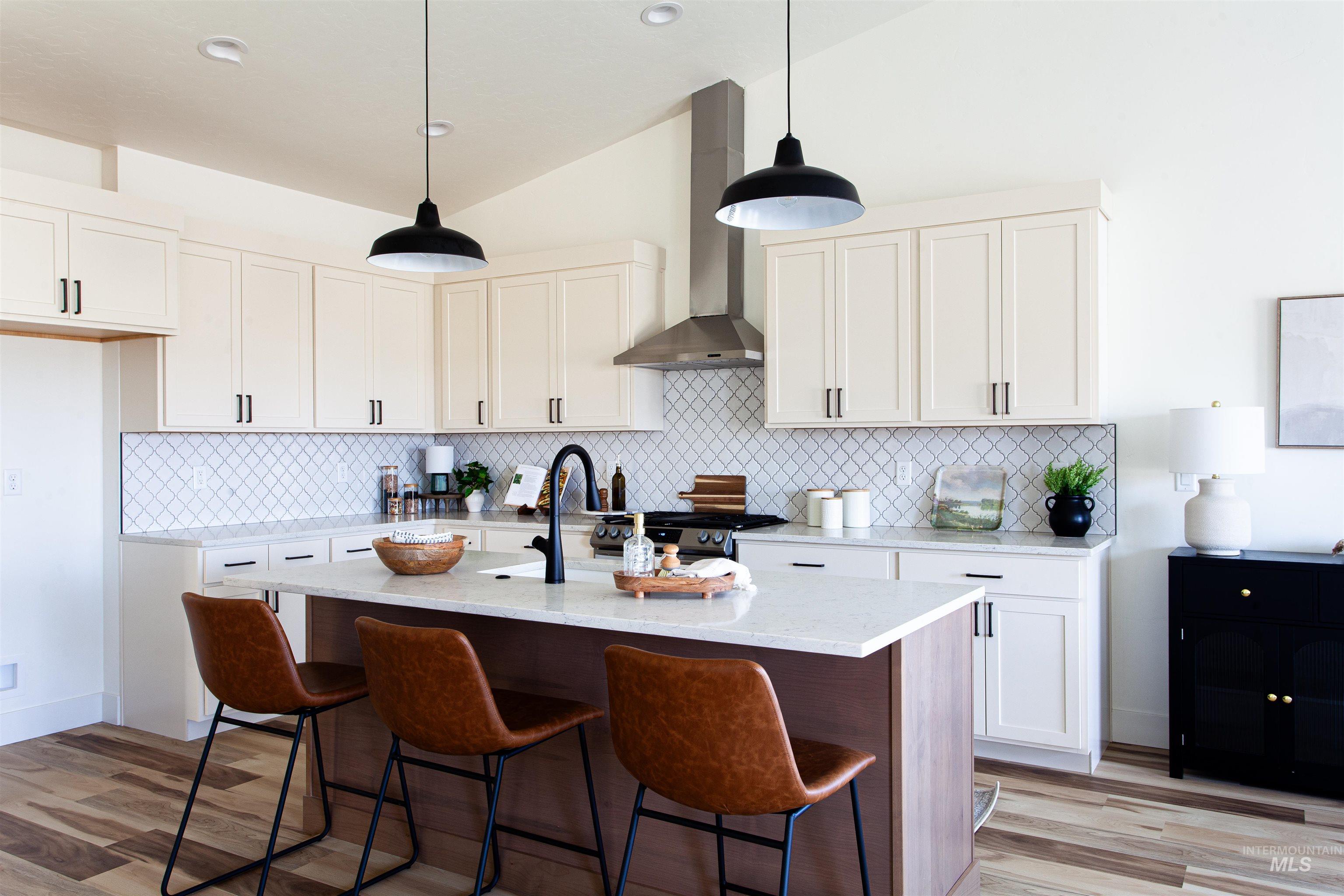 Kitchen with white cabinets, pendant lighting, tasteful backsplash, wall chimney range hood, and vaulted ceiling