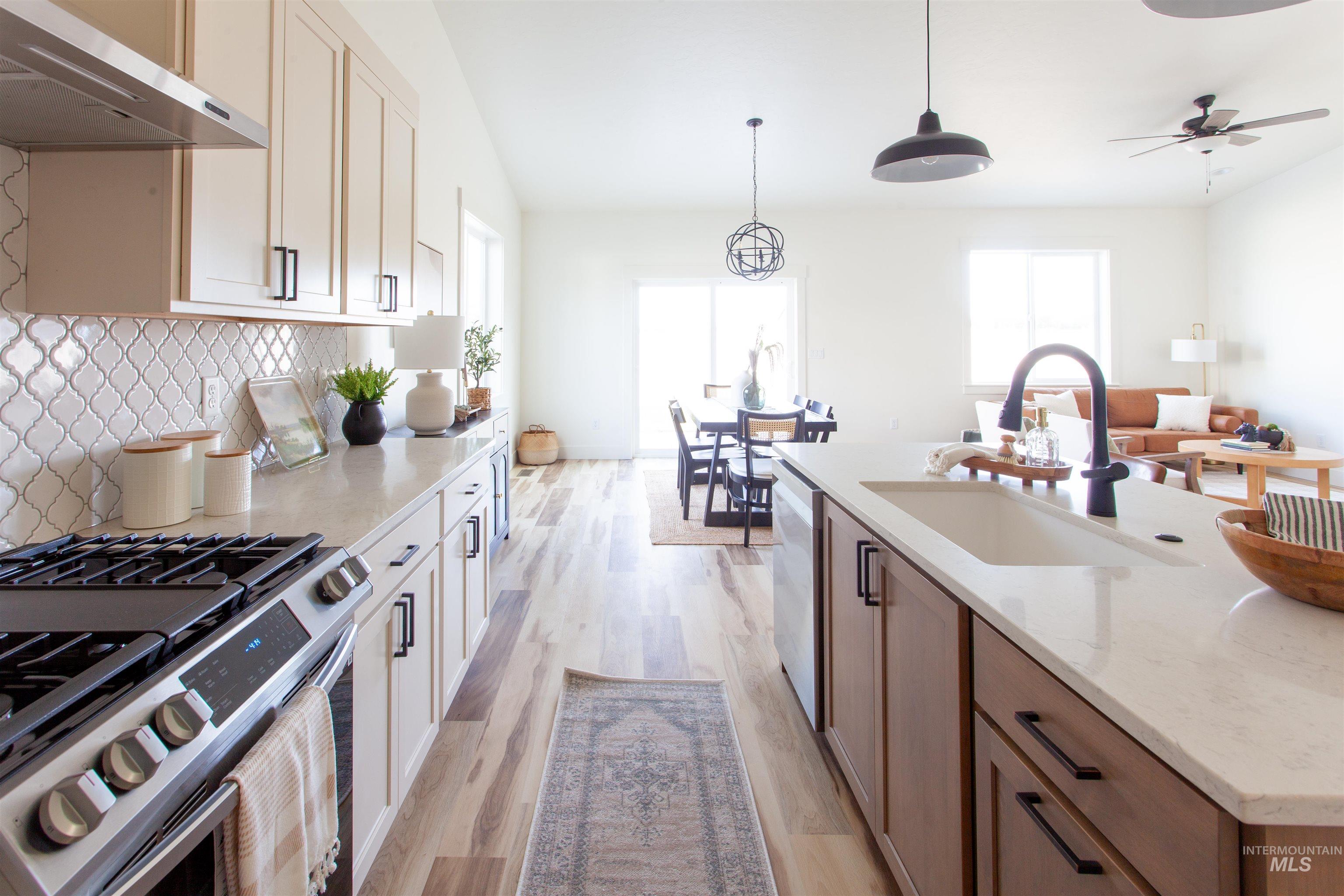 Kitchen with stainless steel appliances, under cabinet range hood, decorative backsplash, light stone counters, and light wood-style floors