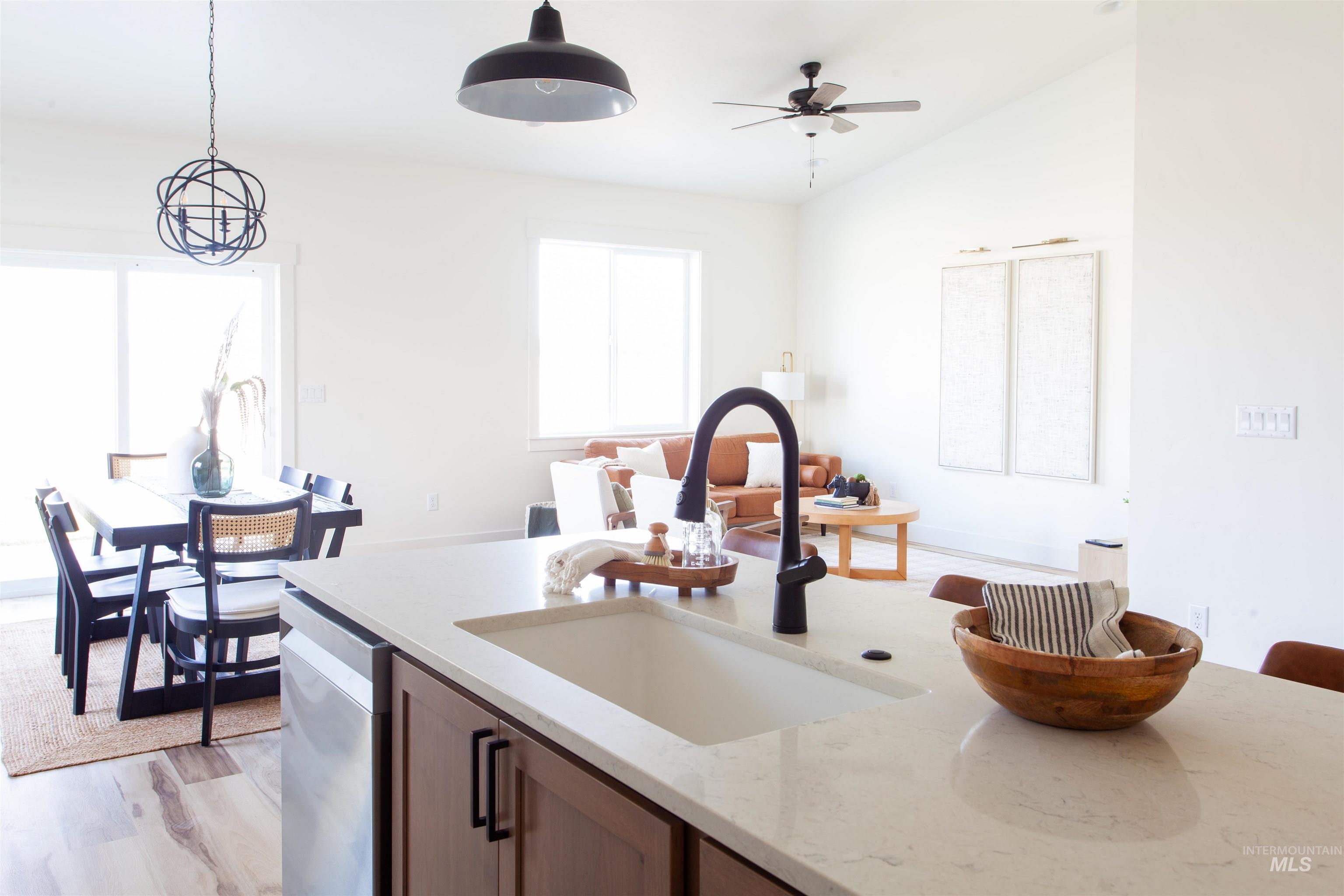 Kitchen featuring light stone countertops, pendant lighting, light wood-style flooring, ceiling fan, and stainless steel dishwasher