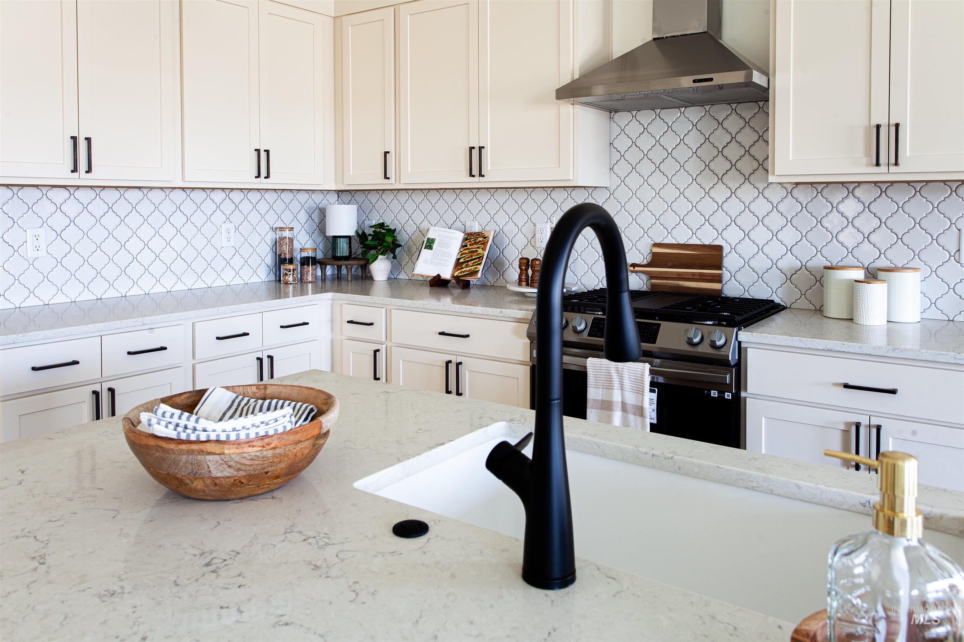 Kitchen featuring ventilation hood, light stone counters, decorative backsplash, and white cabinetry