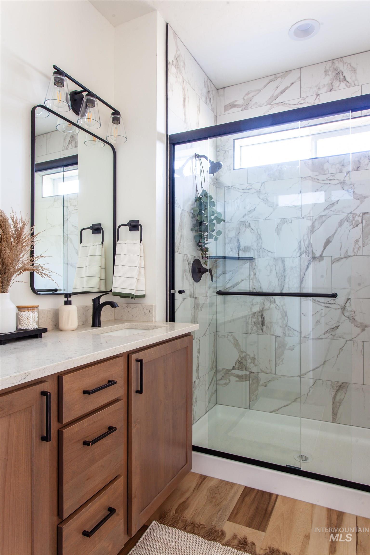 Bathroom featuring vanity, a marble finish shower, and light wood finished floors