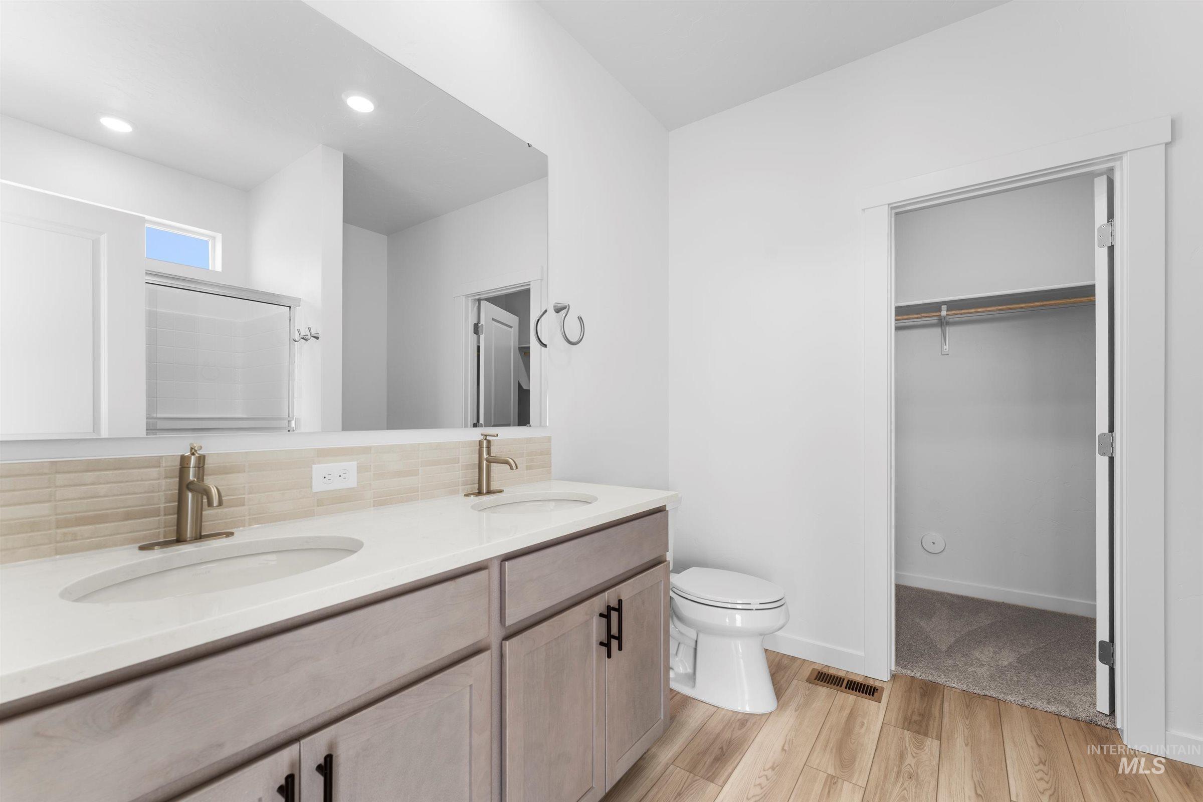 Bathroom with light wood finished floors, double vanity, a stall shower, a spacious closet, and recessed lighting
