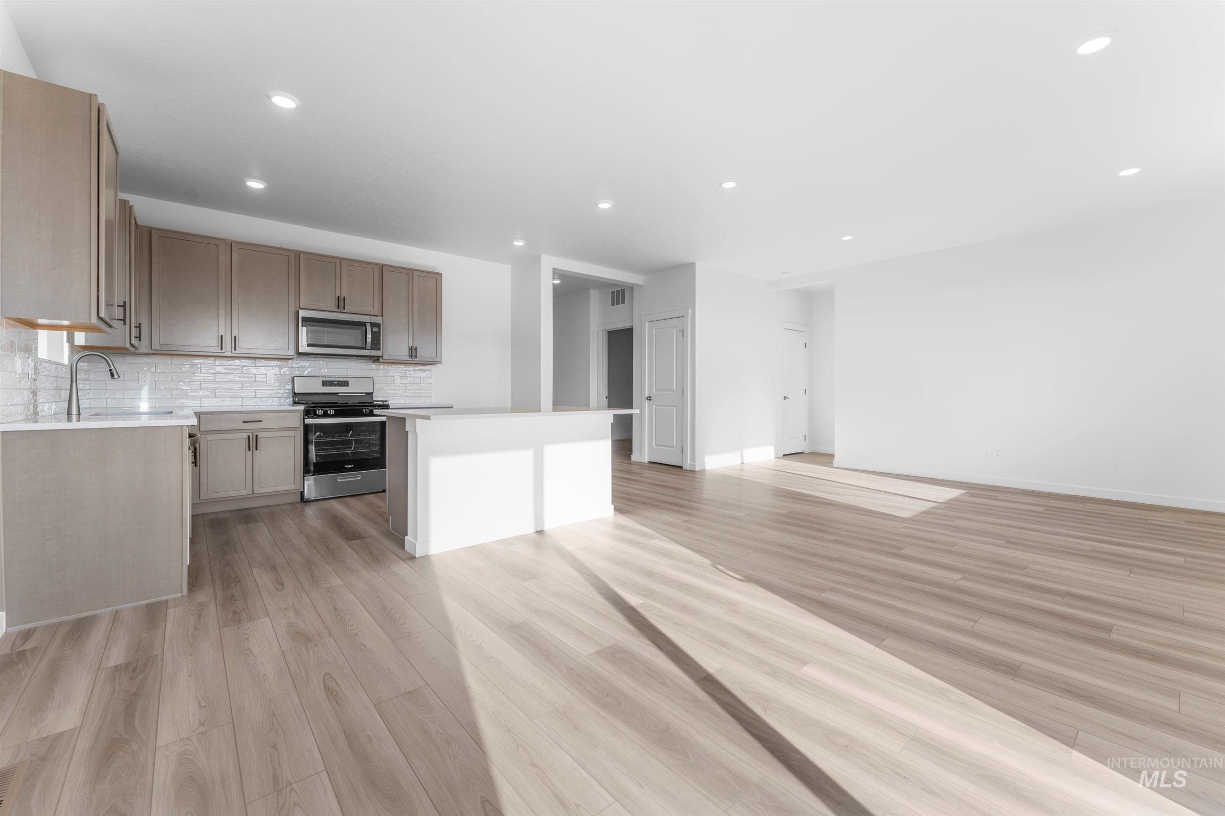 Kitchen with appliances with stainless steel finishes, decorative backsplash, light wood-style flooring, open floor plan, and recessed lighting