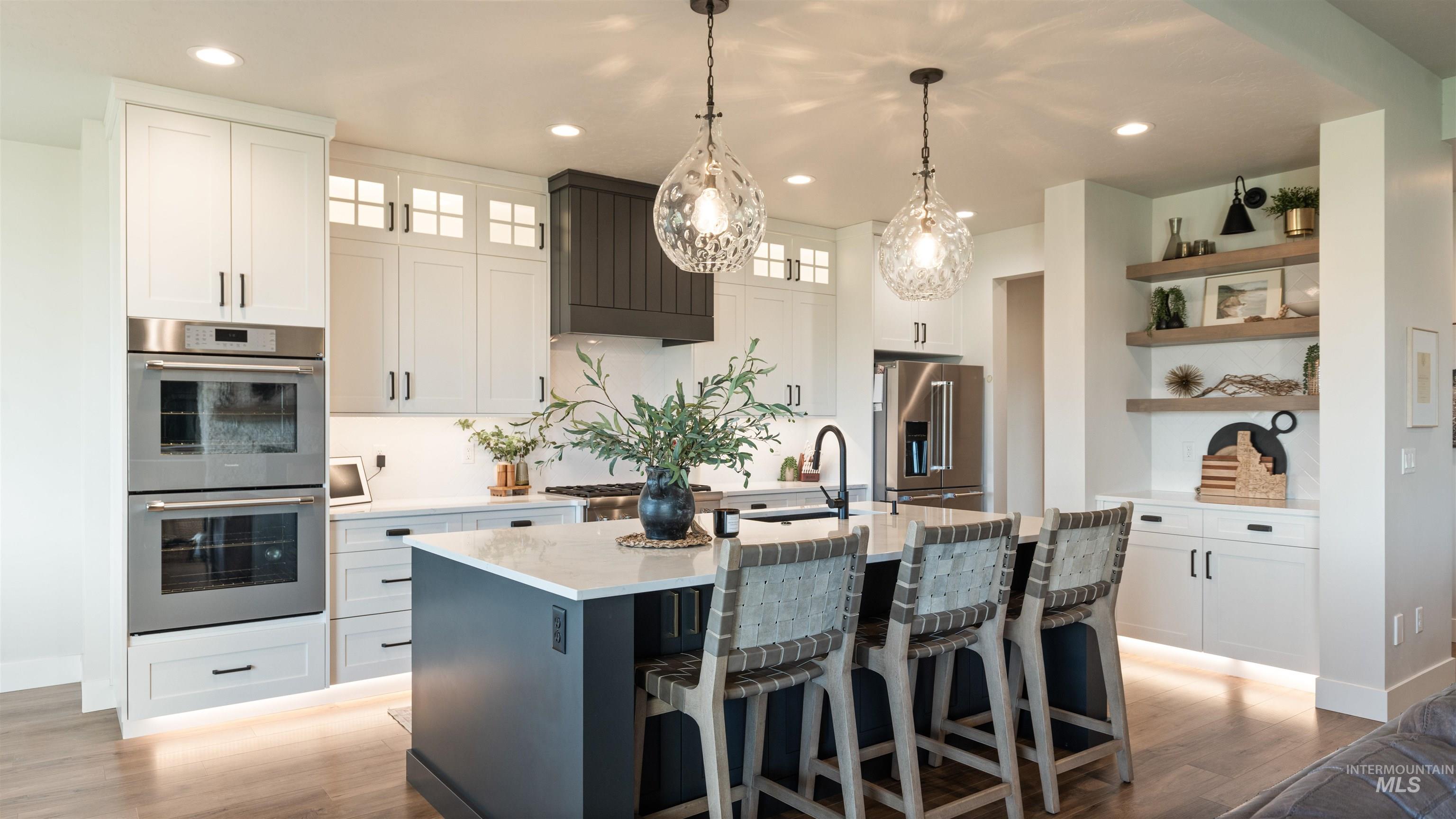 Kitchen featuring stainless steel appliances, light wood-style flooring, dual tone cabinets, decorative light fixtures, and light stone counters
