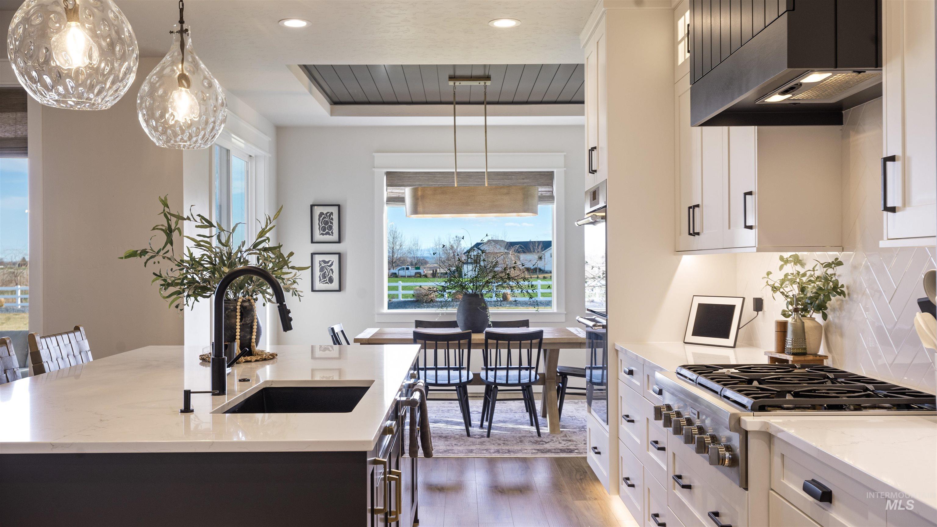 Dual tone kitchen featuring light stone countertops, stainless steel appliances, dual tone cabinets, a kitchen island with sink, and dark wood finished floors