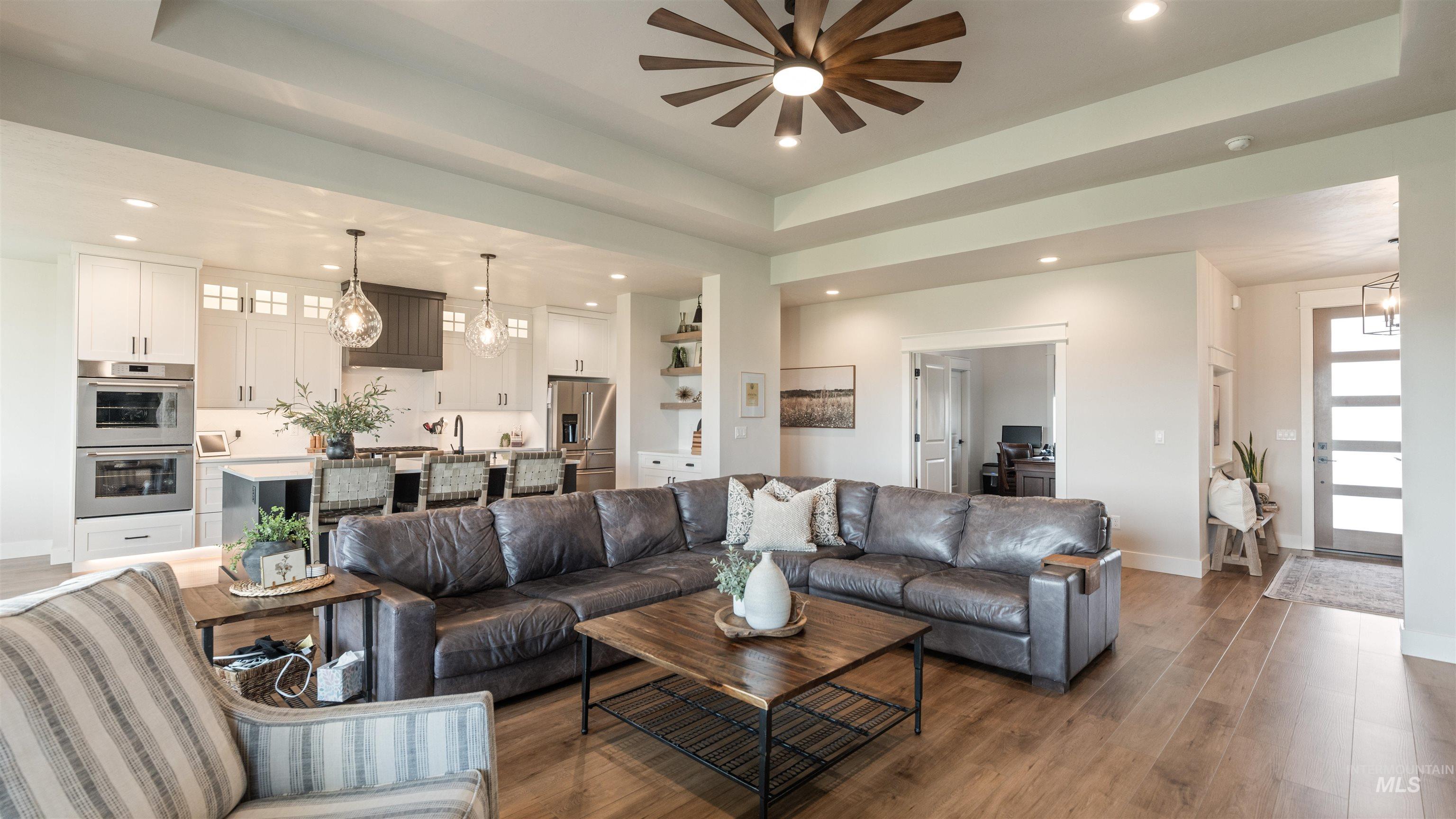 Living room with a tray ceiling, light wood finished floors, suspended lighting, and ceiling fan