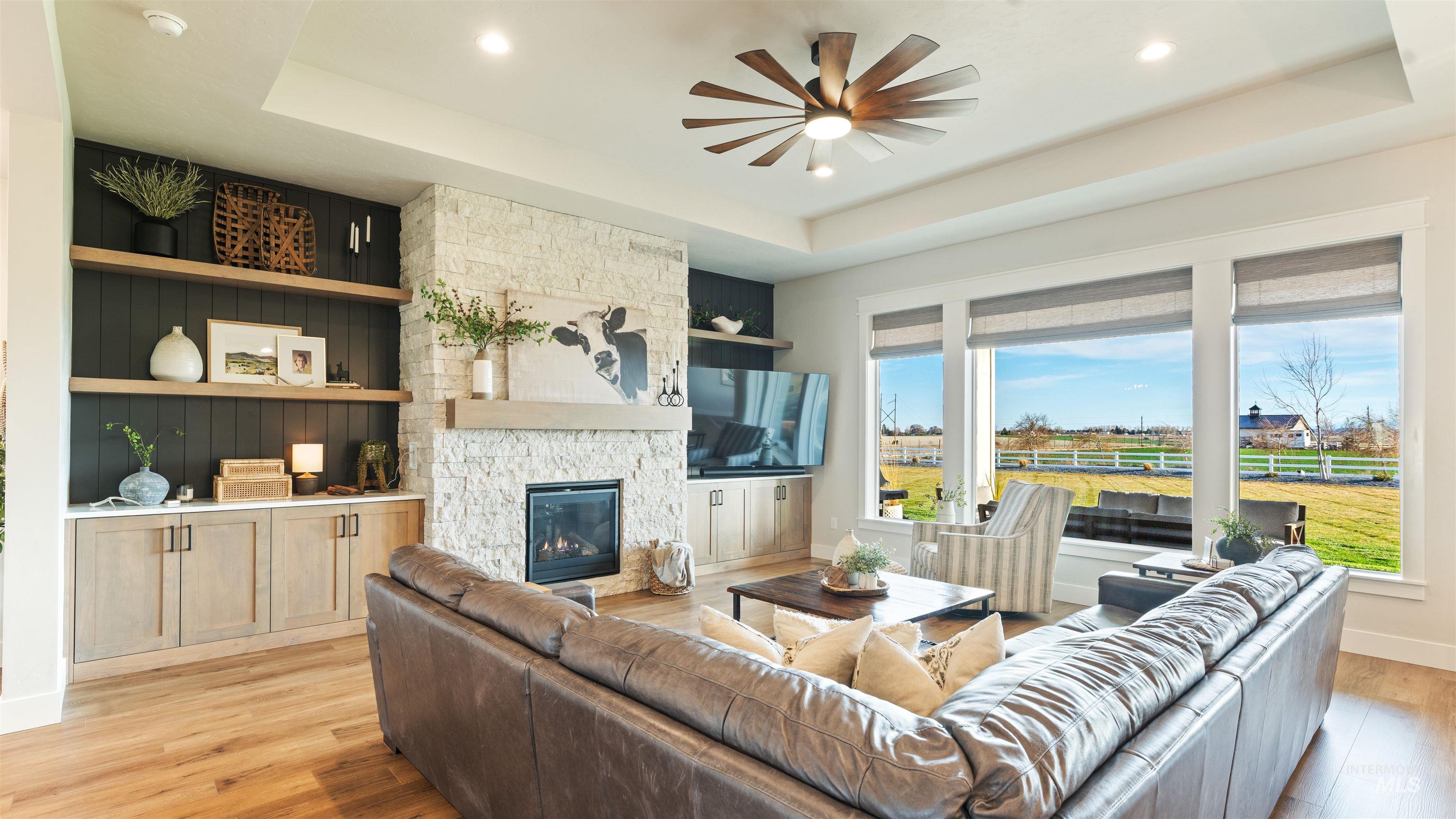 Living room featuring a raised ceiling, light wood-style flooring, a ceiling fan, a fireplace, and recessed lighting