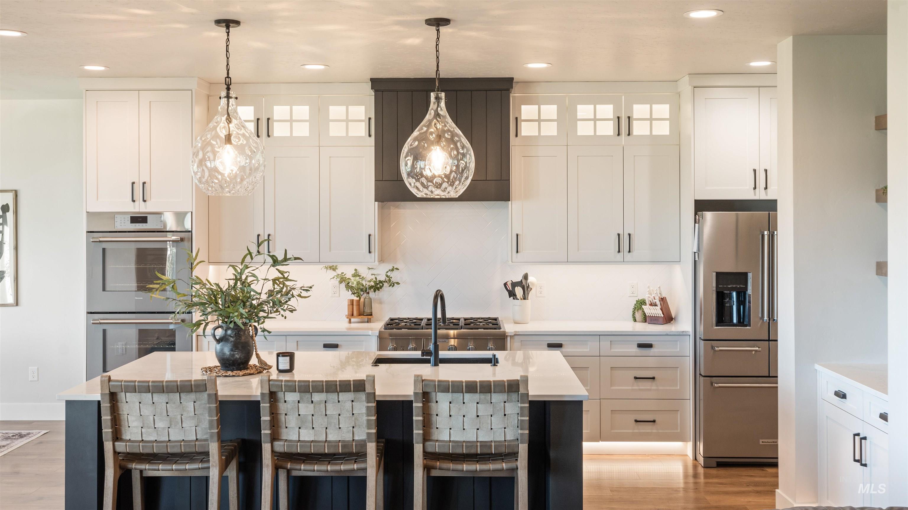 Kitchen featuring white cabinets, stainless steel appliances, a kitchen breakfast bar, a kitchen island with sink, and decorative light fixtures