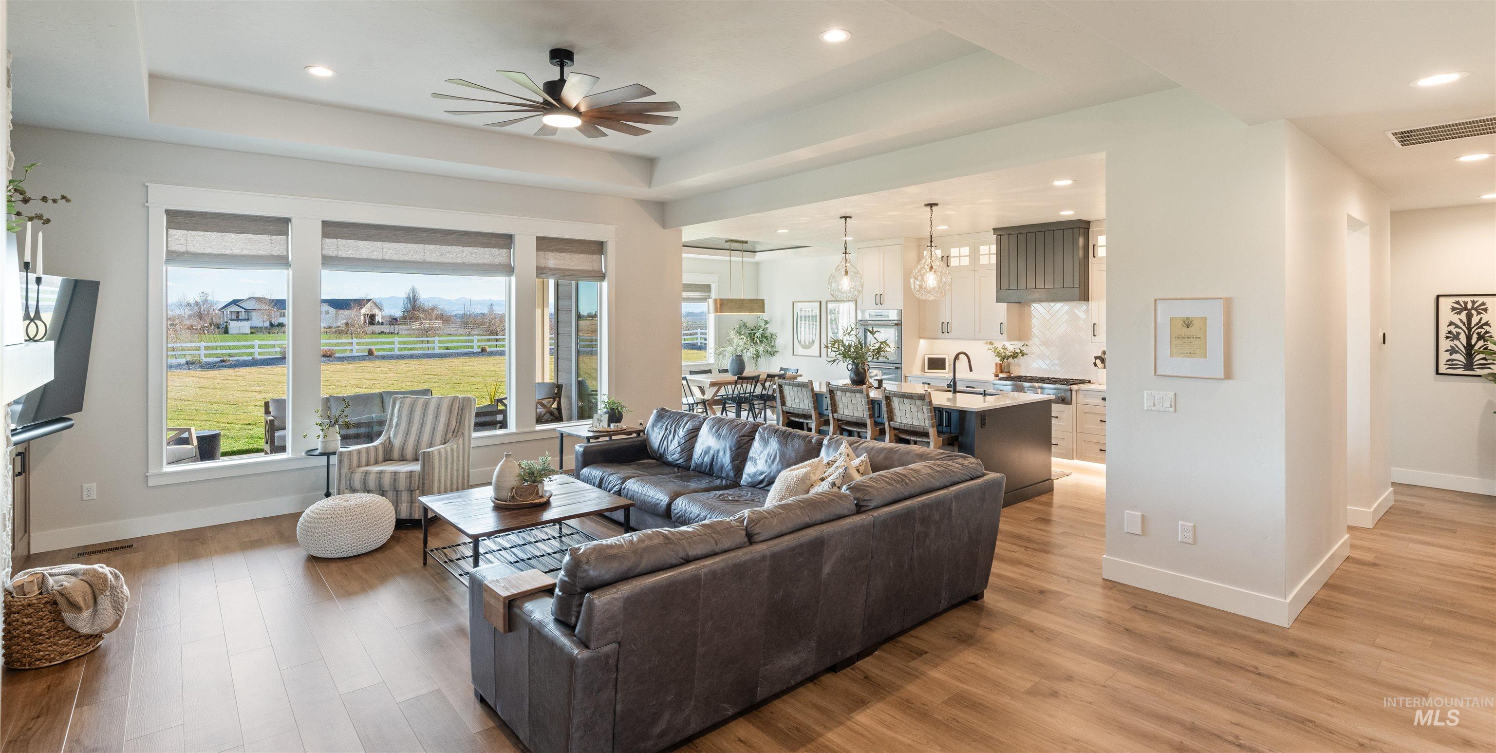 Living room with ceiling fan, light wood finished floors, recessed lighting, and a tray ceiling