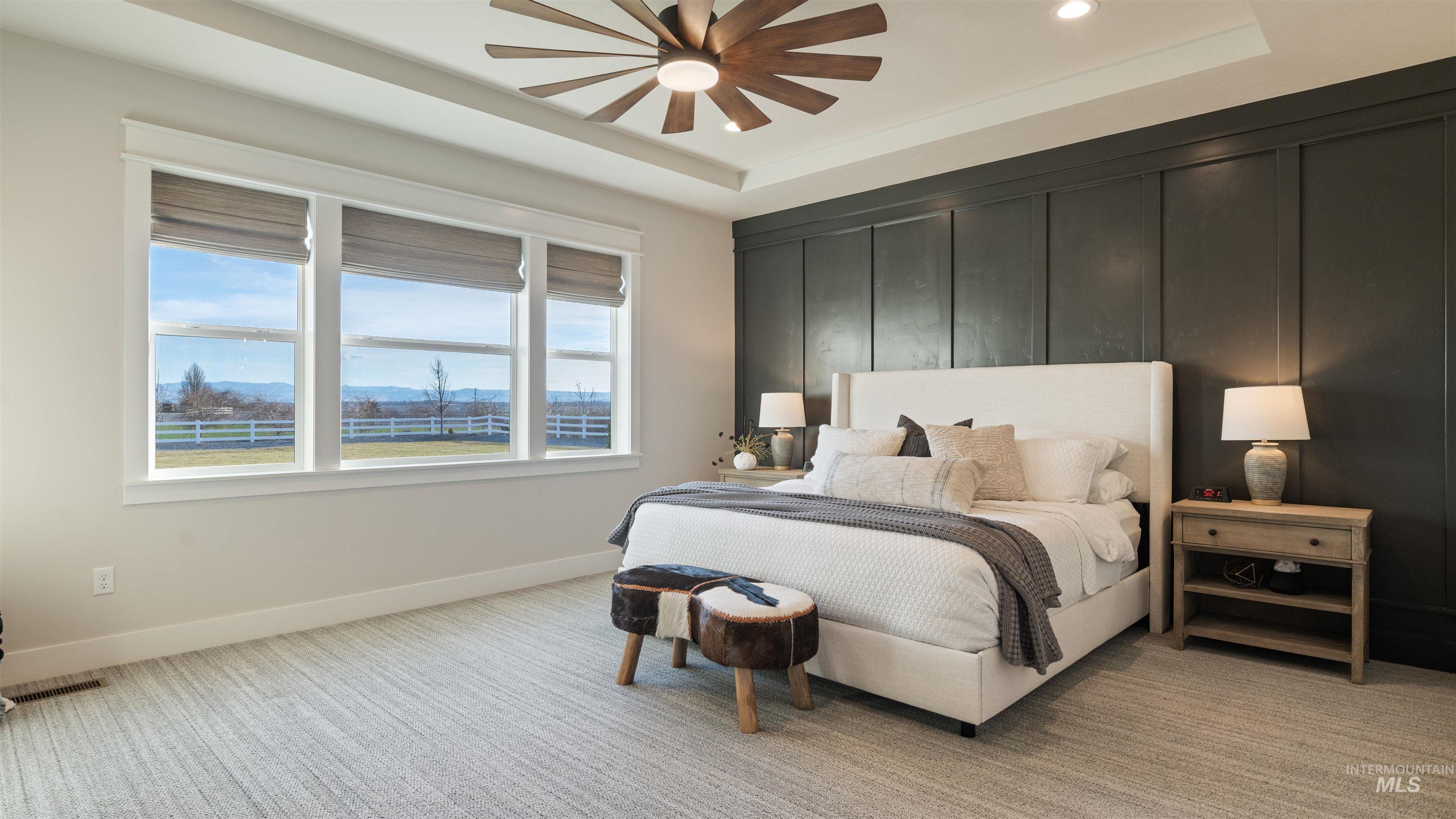 Bedroom with a mountain view, a tray ceiling, light carpet, and a ceiling fan